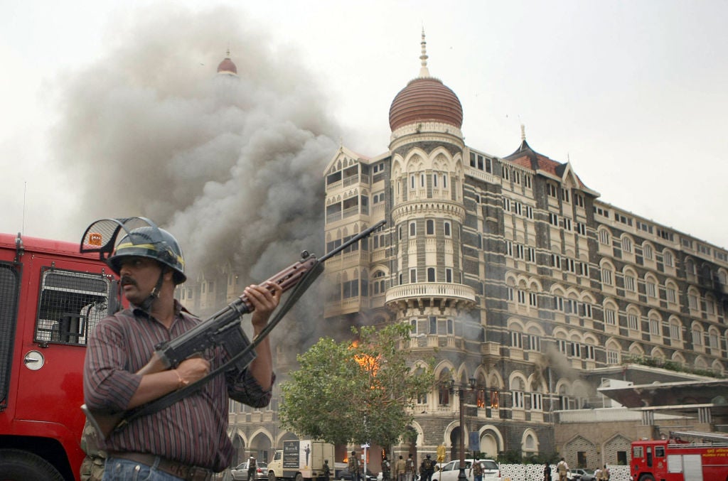 <p>File: An Indian security official stands alert as smoke and flames billow out from The Taj Mahal hotel during the Mumbai terrorist attacks in November 2008</p>