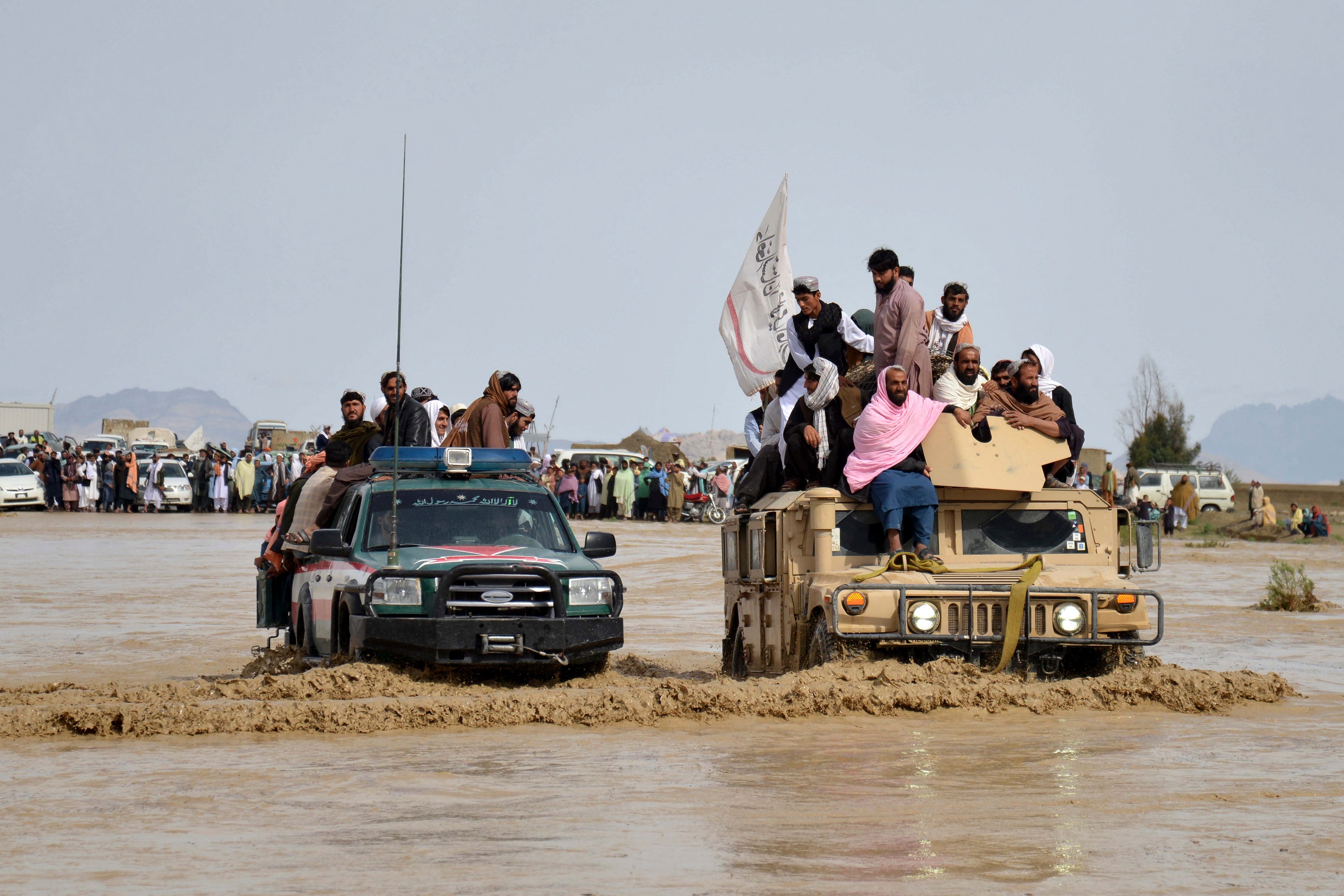 Afghan men sit atop military vehicles as they cross a flooded area in Kandahar province on Saturday