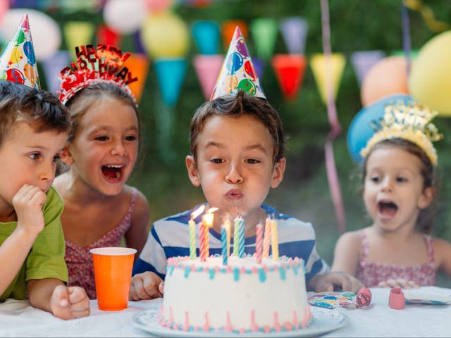 <p>Little boy blowing birthday candles at an outdoor birthday party in the yard.</p>