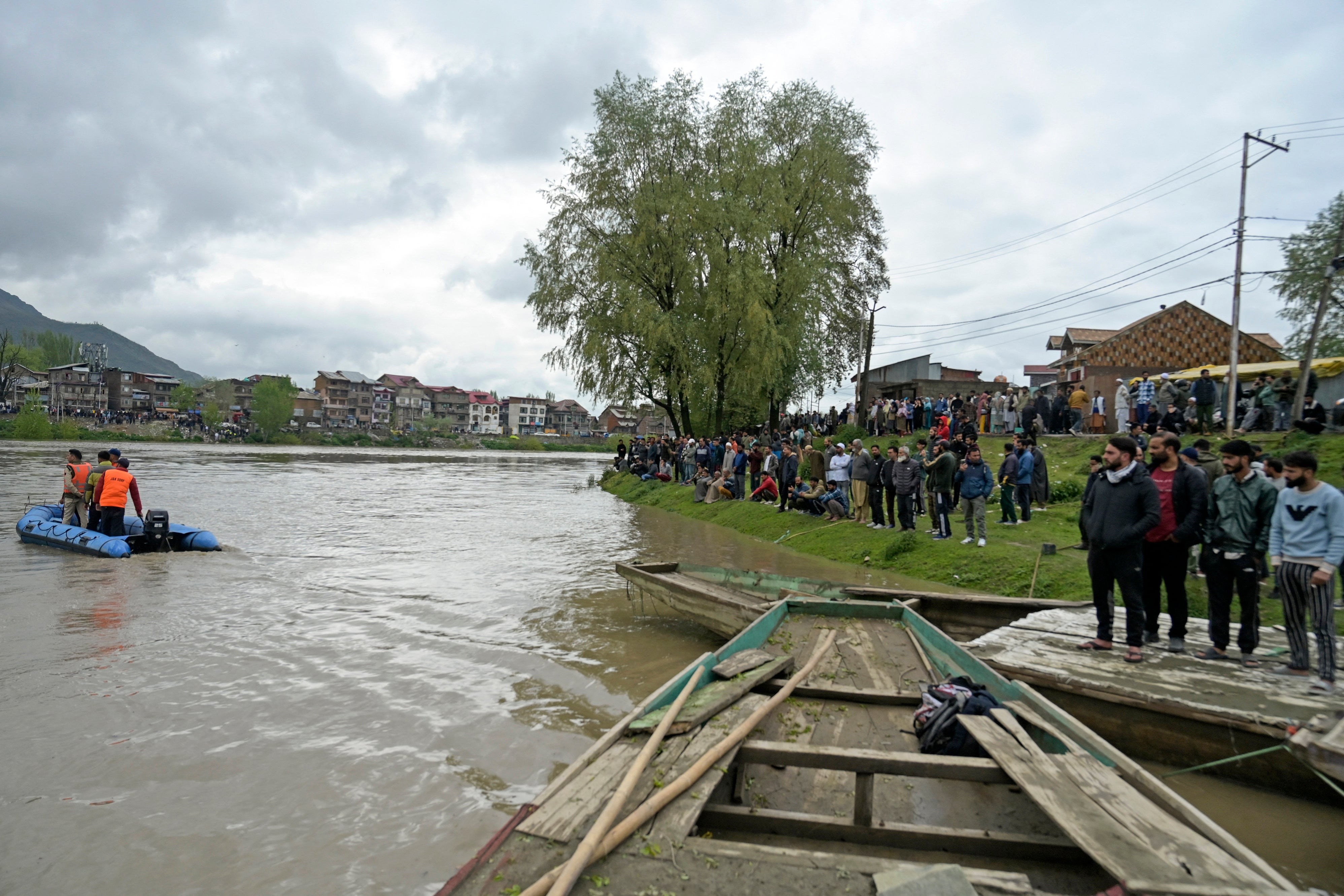 People gather along the bank of the Jhelum river as National Disaster Response Force (NDRF) personnel (L) conduct a rescue and search operation after a boat ferrying people capsized in Srinagar