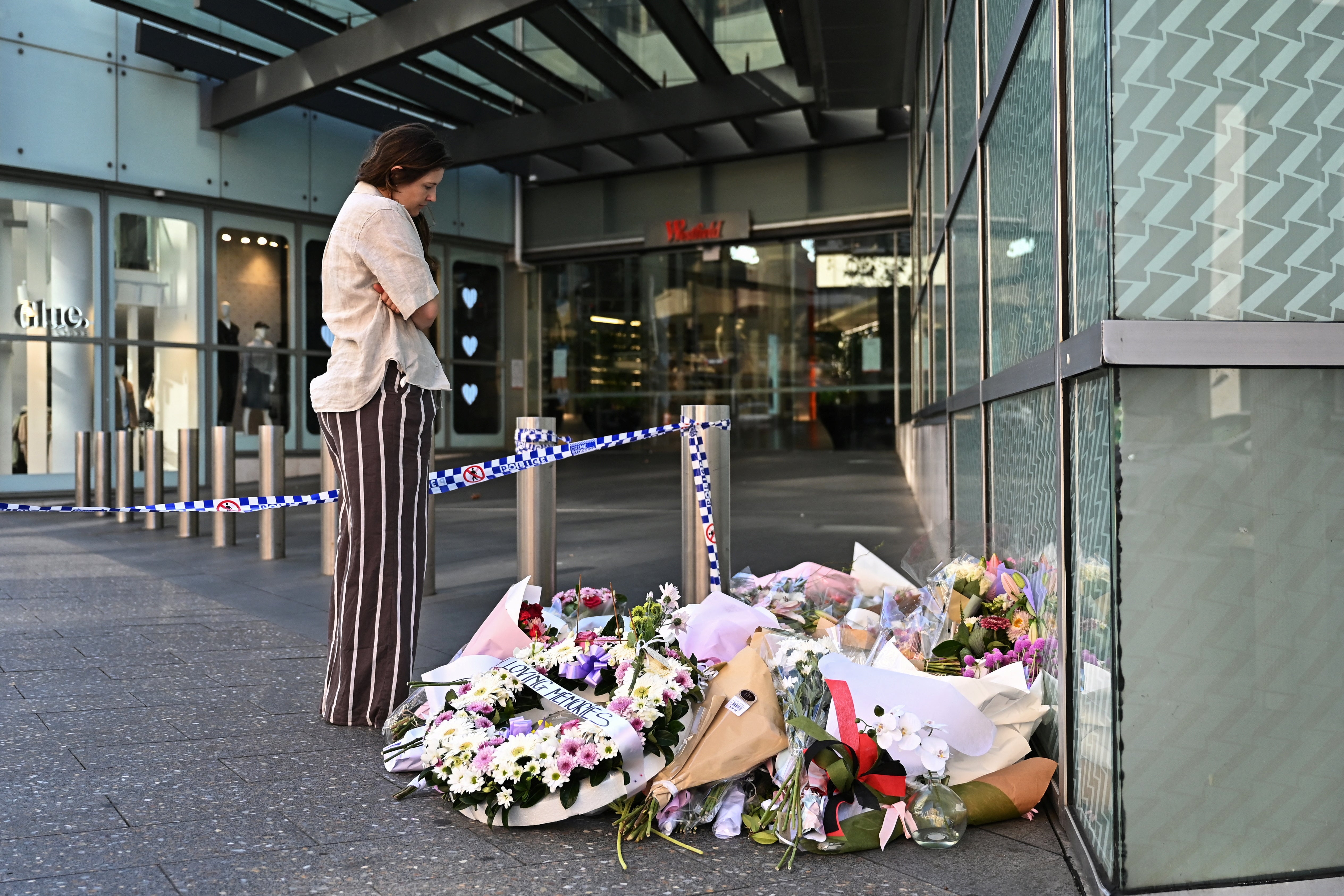A person looks at floral tributes for victims of the attack left at the entrance to Westfield Bondi Junction shopping centre in Sydney