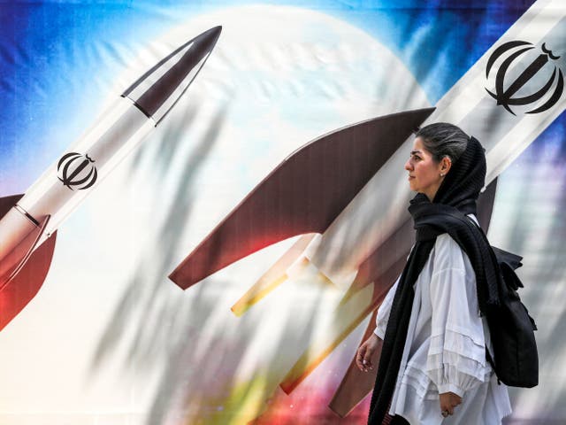 <p>A woman in Tehran walks past a mural depicting missiles being launched </p>