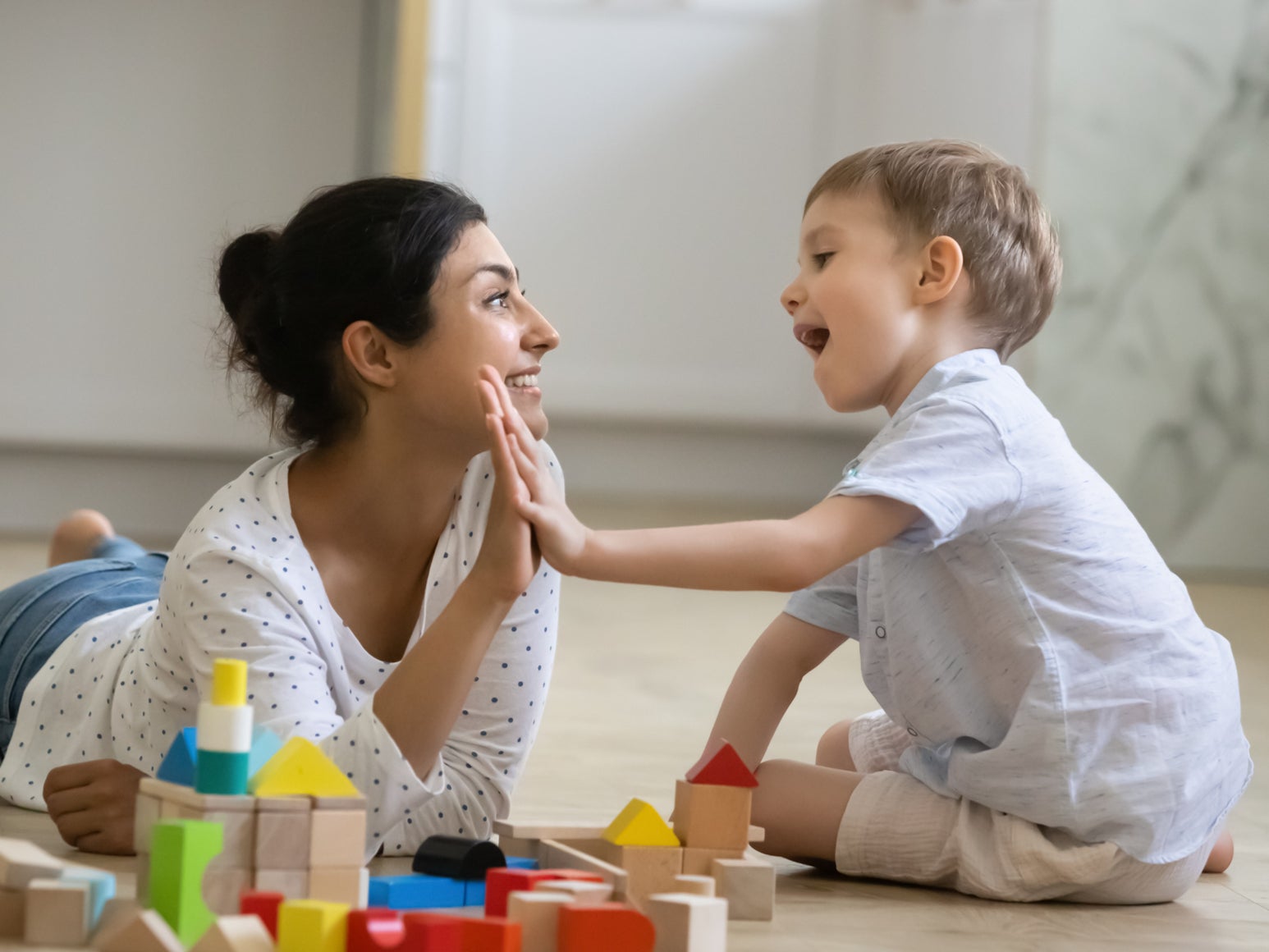 <p>A happy nanny giving high-five praise to an excited preschool kid boy for completing a toy tower on the floor. </p>