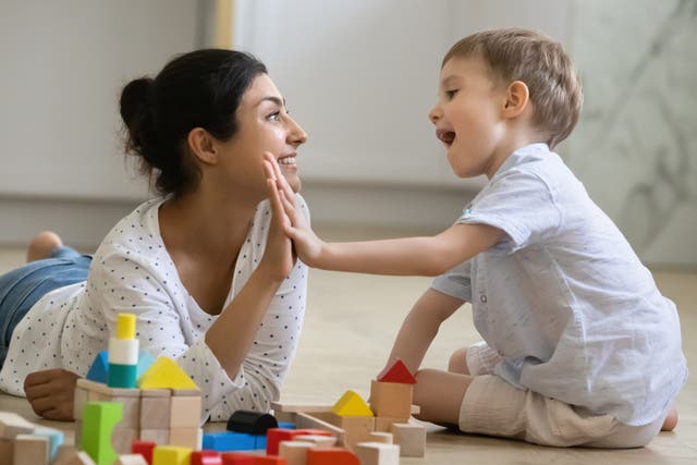 <p>A happy nanny giving high-five praise to an excited preschool kid boy for completing a toy tower on the floor. </p>