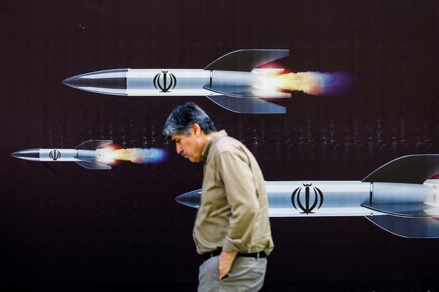 <p>A man walks past a banner depicting missiles on a street in Tehran </p>