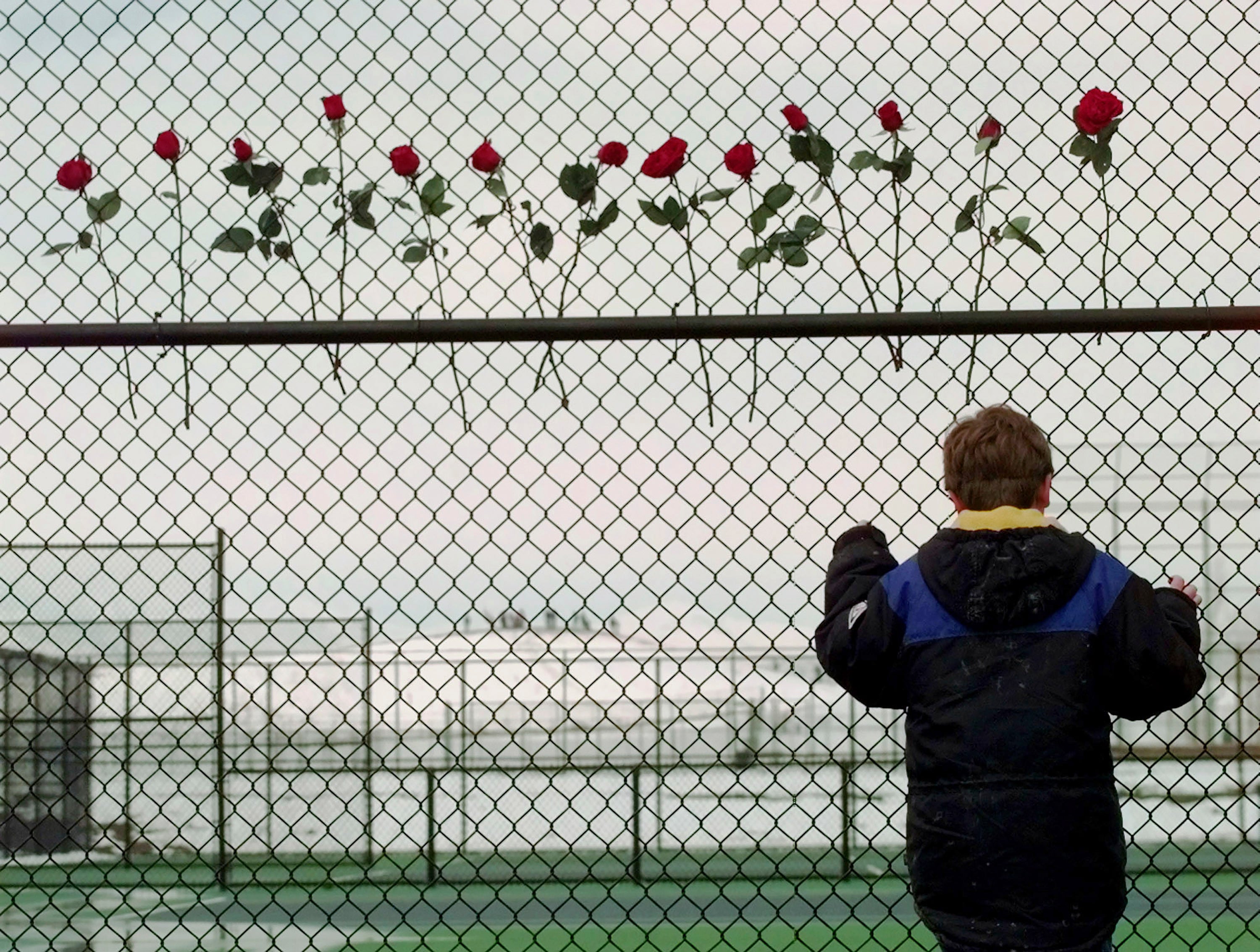 A boy looks through the fence at the Columbine High School tennis courts four days after the attack by two student shooters that killed 12 teens and one teacher, injuring 24 more