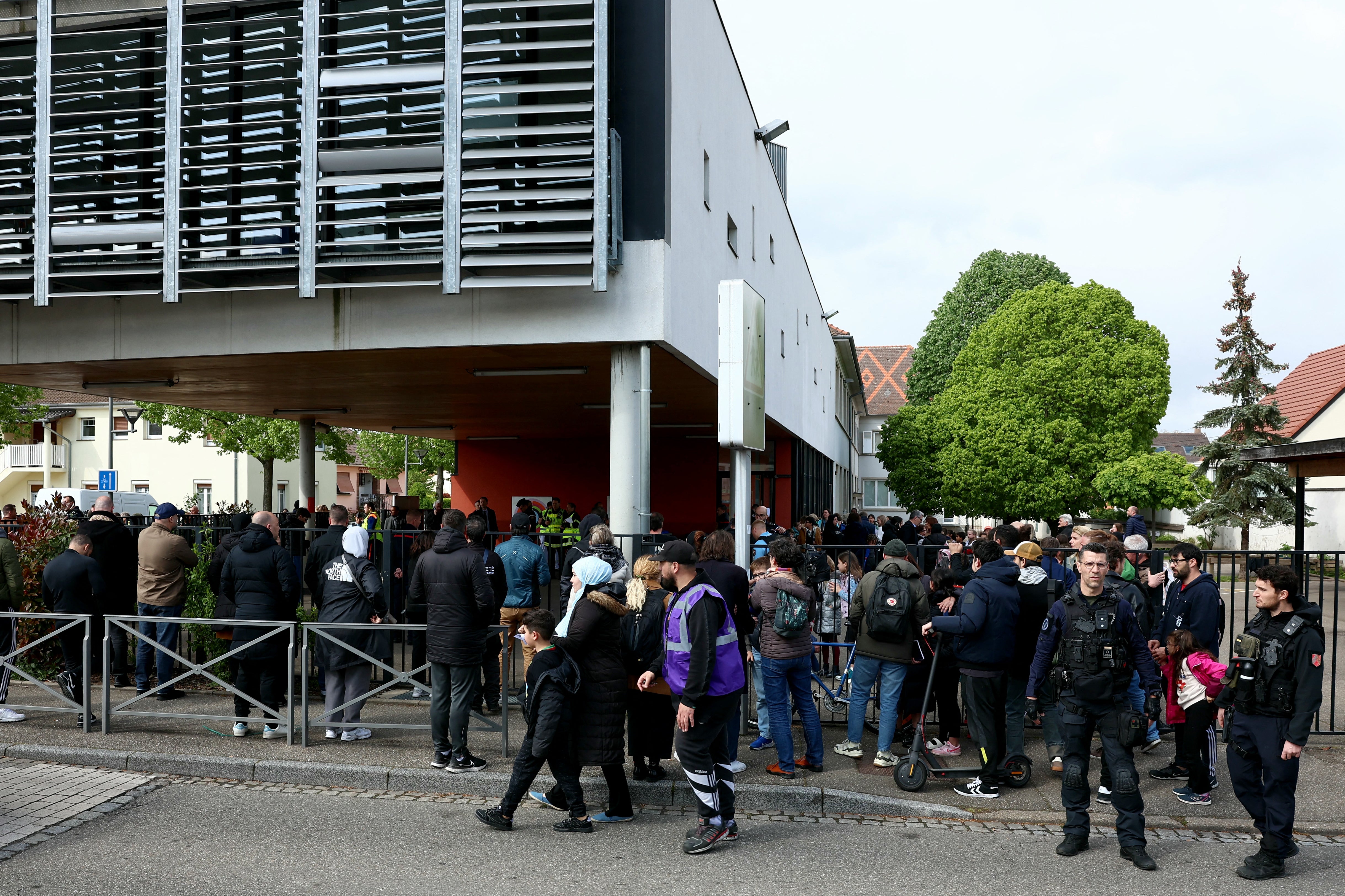 Pupils and parents gather outside a school among police forces in the eastern France city of Souffelweyersheim after two girls were wounded in a knife attack outside the school on Thursday