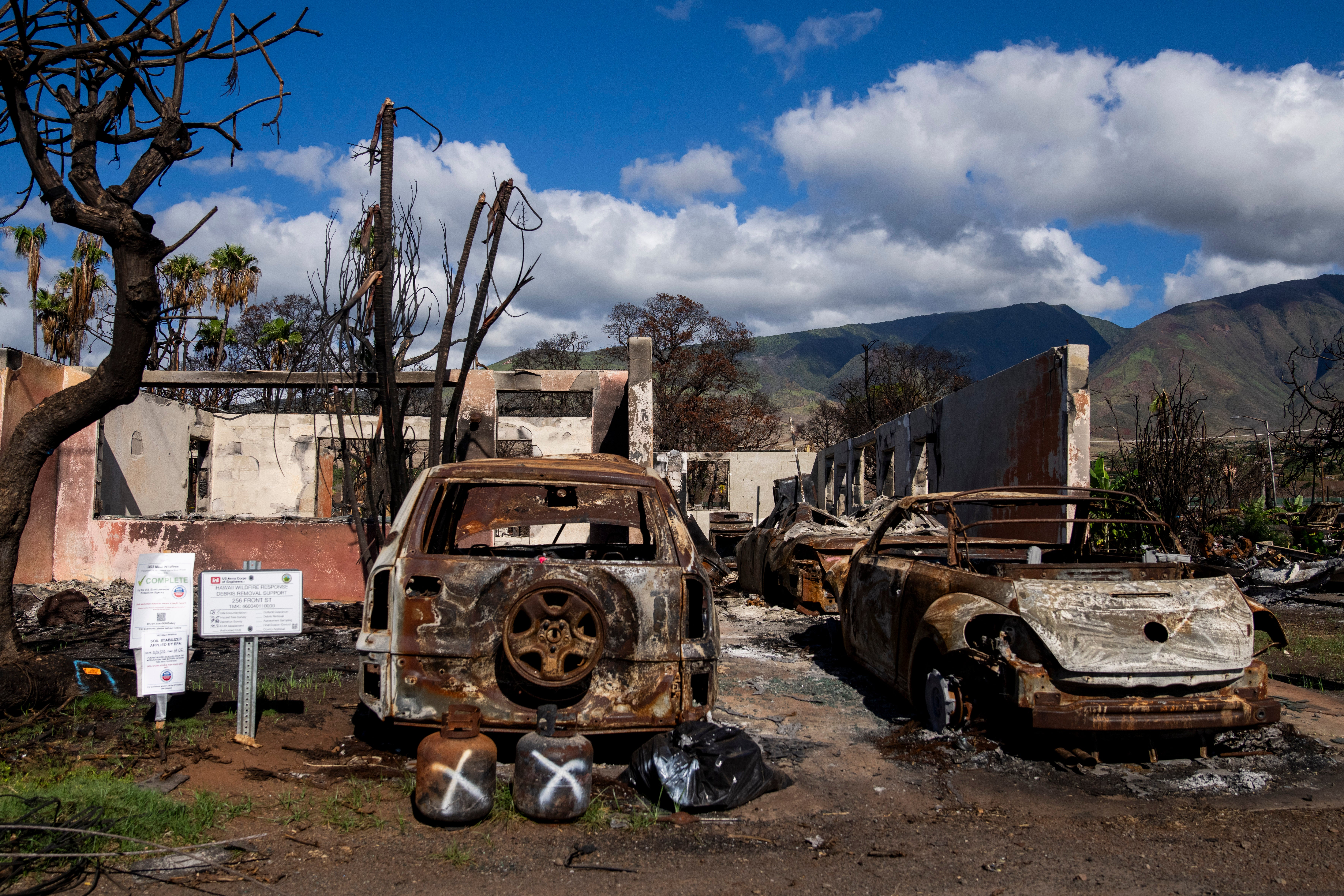 Burned cars and propane tanks with markings on them sit outside a house destroyed by wildfire, Friday, Dec. 8, 2023, in Lahaina, Hawaii. An acute housing shortage hitting fire survivors on the Hawaiian island of Maui is squeezing out residents even as they try to overcome the loss of loved ones, their homes and their community