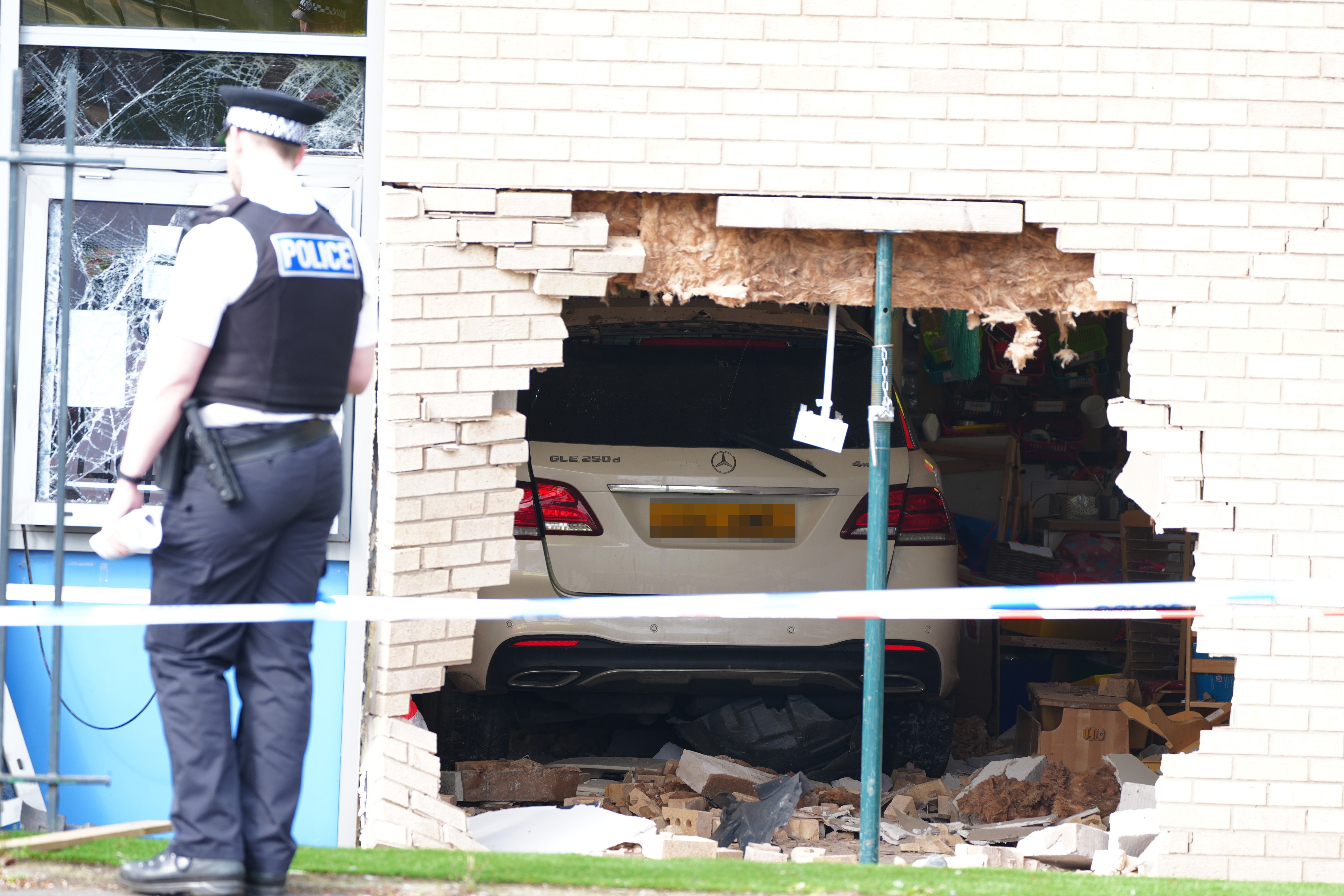 Police officers stand next to the damage after the Mercedes appeared to have crashed through the wall into a classroom