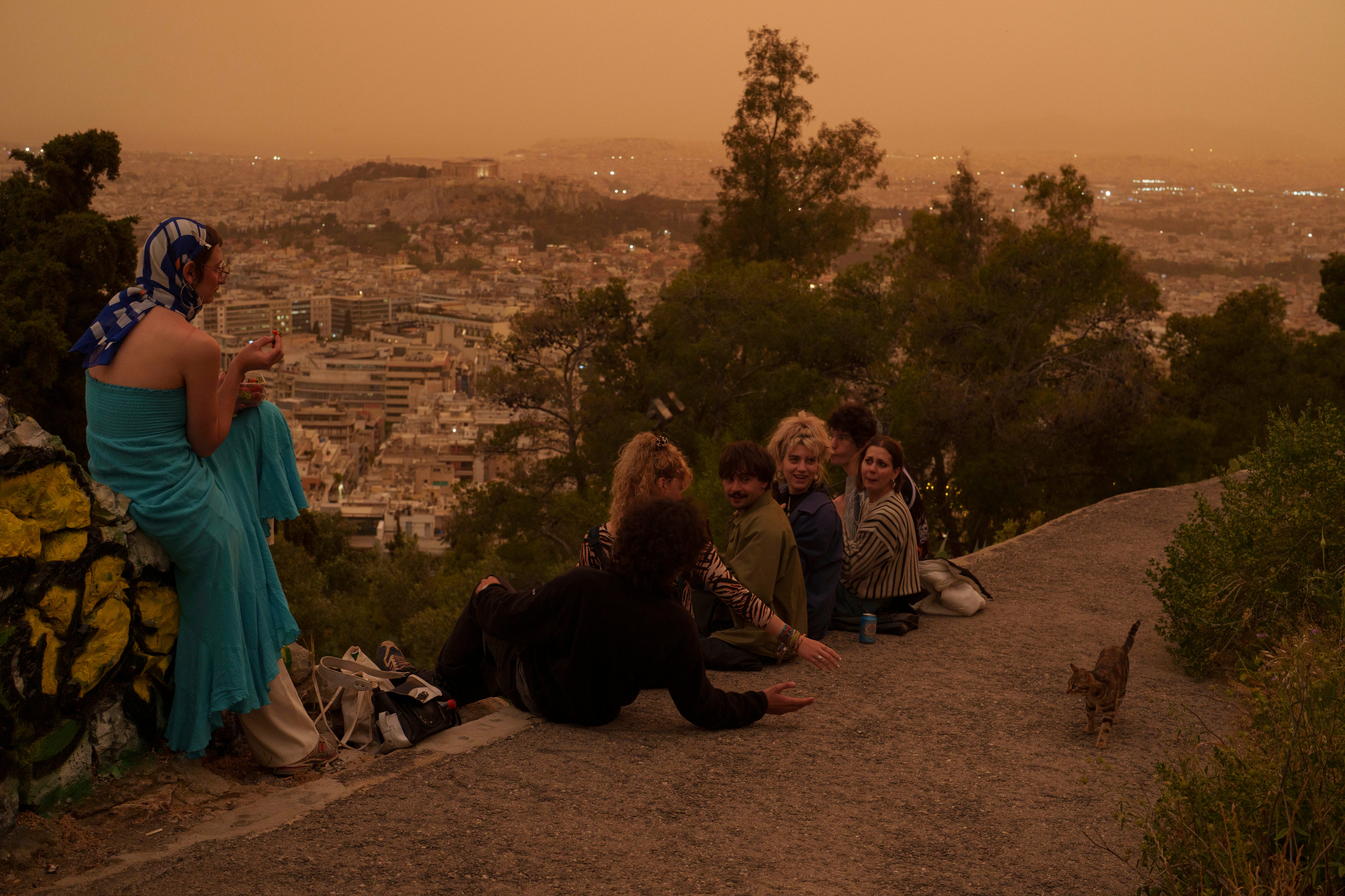 Tourists play with a cat at Lycabettus hill as the city of Athens with the ancient Acropolis hill is seen at the background