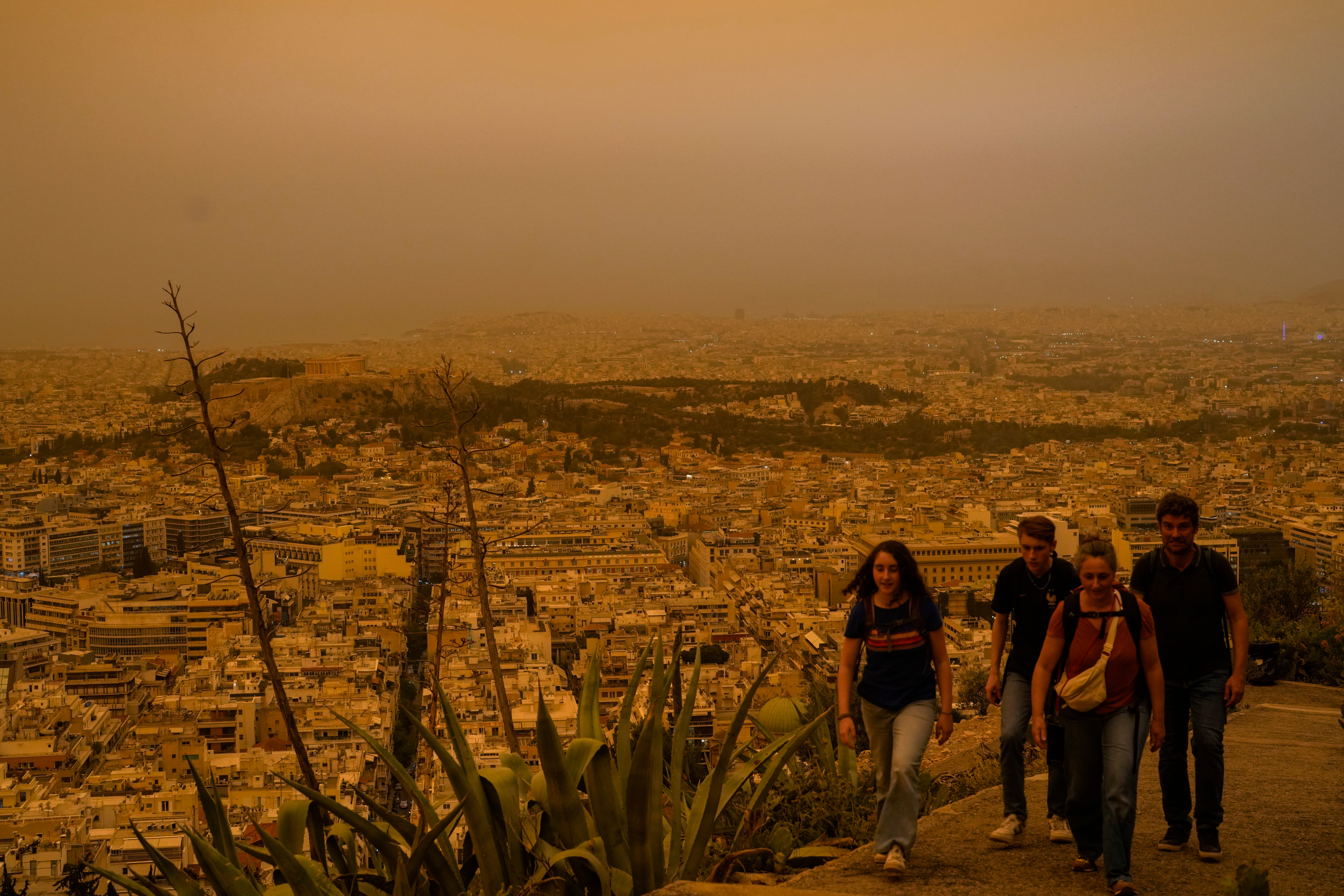 Tourists walk at the Lycabettus hill as the city of Athens with the ancient Acropolis hill is seen at the background