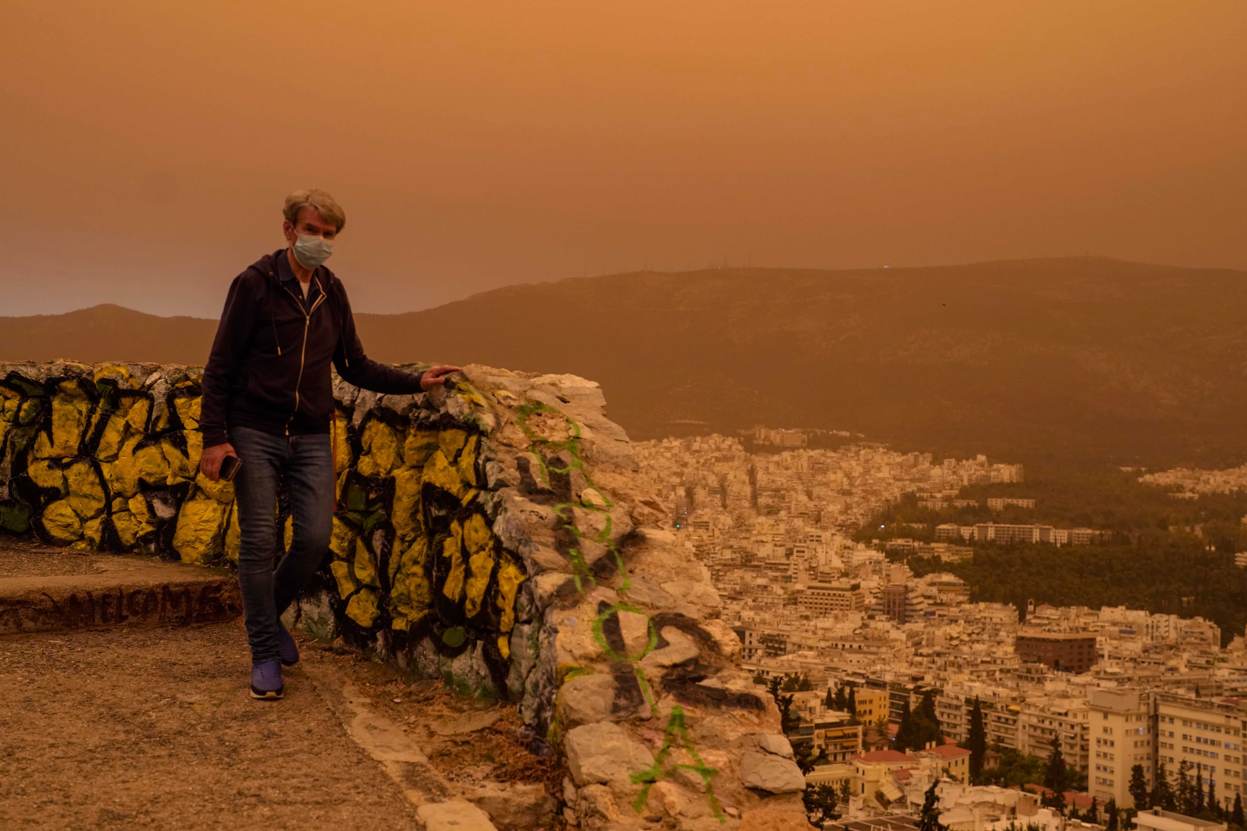 A man wearing a mask walks at the Lycabettus hill as the city of Athens is seen at the background, on Tuesday, April 23