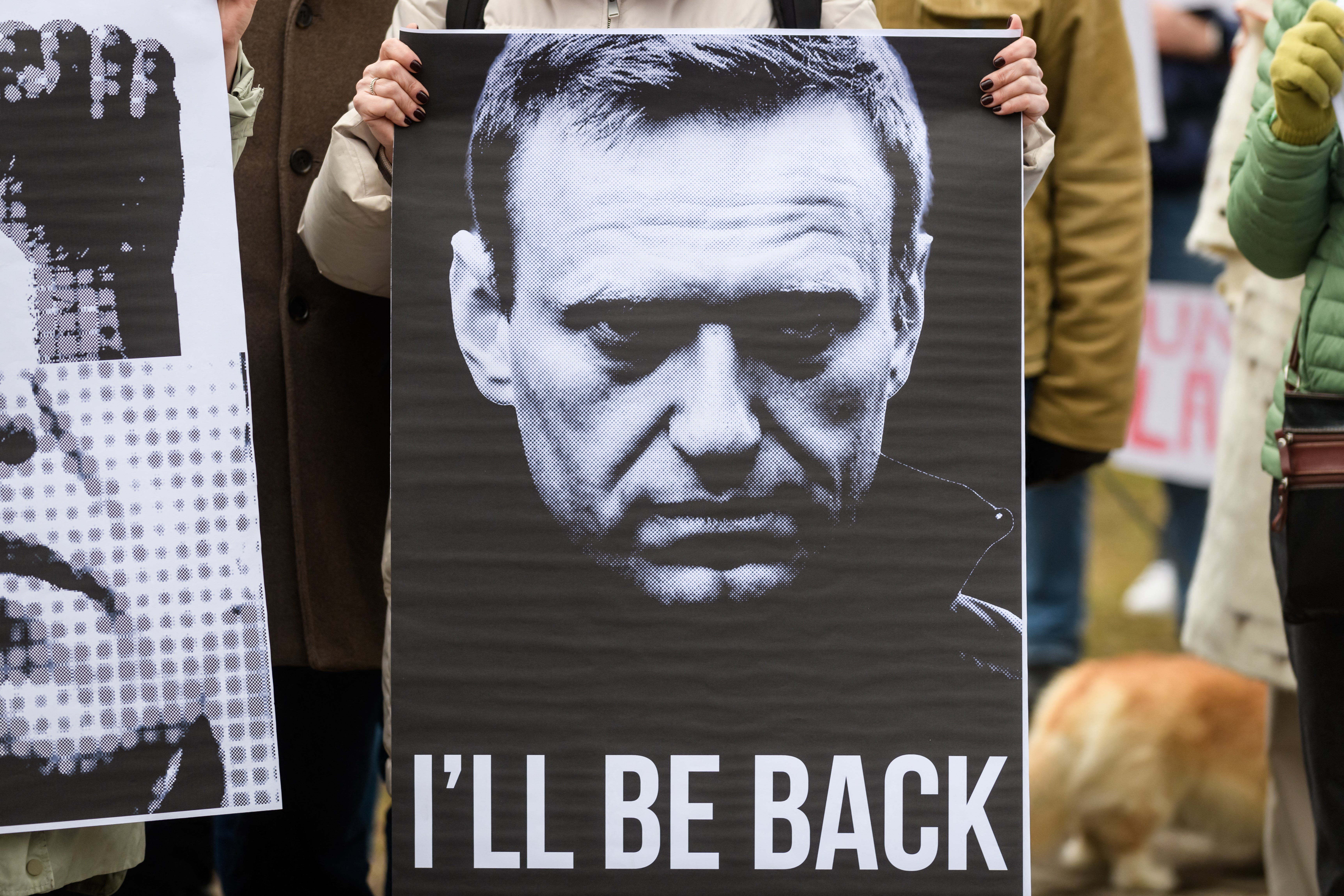 A protester holds a sign depicting late Kremlin opposition leader Alexei Navalny and reading 'I'll be back', during a protest in Riga