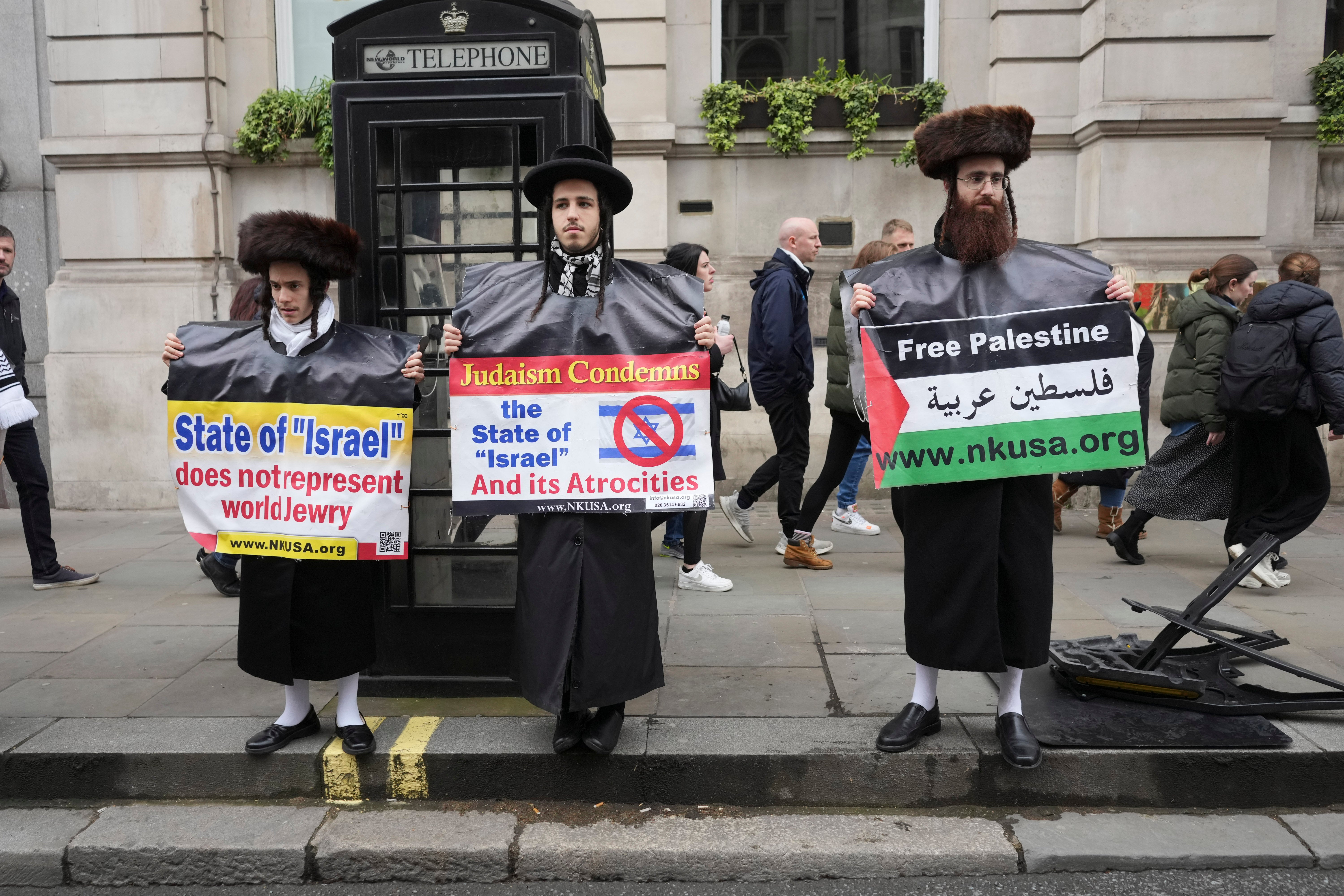 Three Jewish men who belong to the Neturei Karta sect holding placards reading “Judaism condemns the state of Israel”