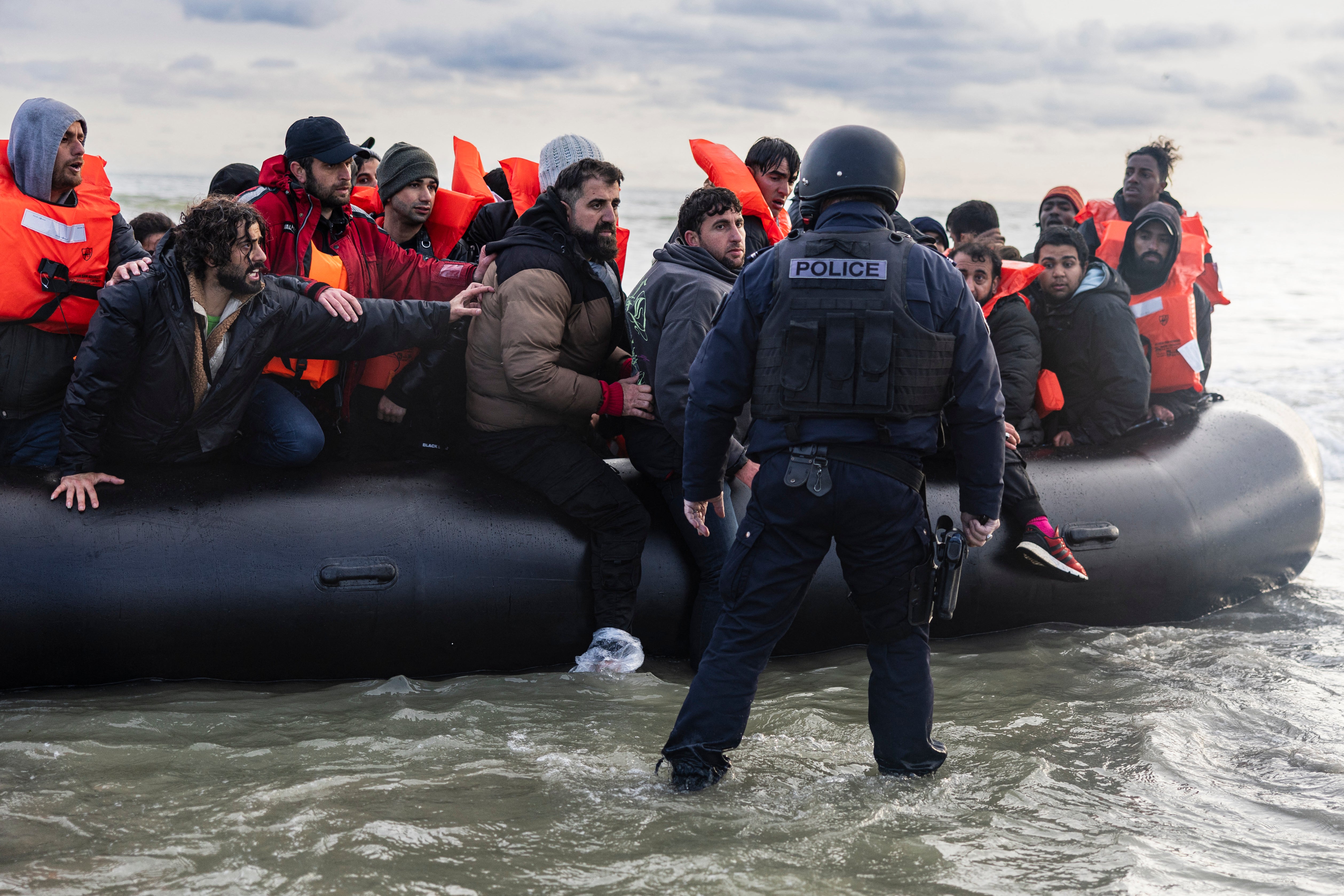 Migrants react as a French police officer stands by ready to puncture the smuggler’s boat to prevent migrants from embarking in an attempt to cross the English Channel