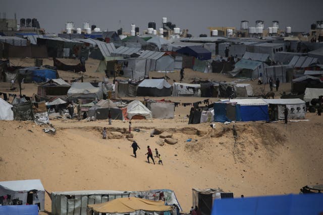 <p>Palestinians walk in a camp for displaced people in Rafah in southern Gaza by the border with Egypt</p>