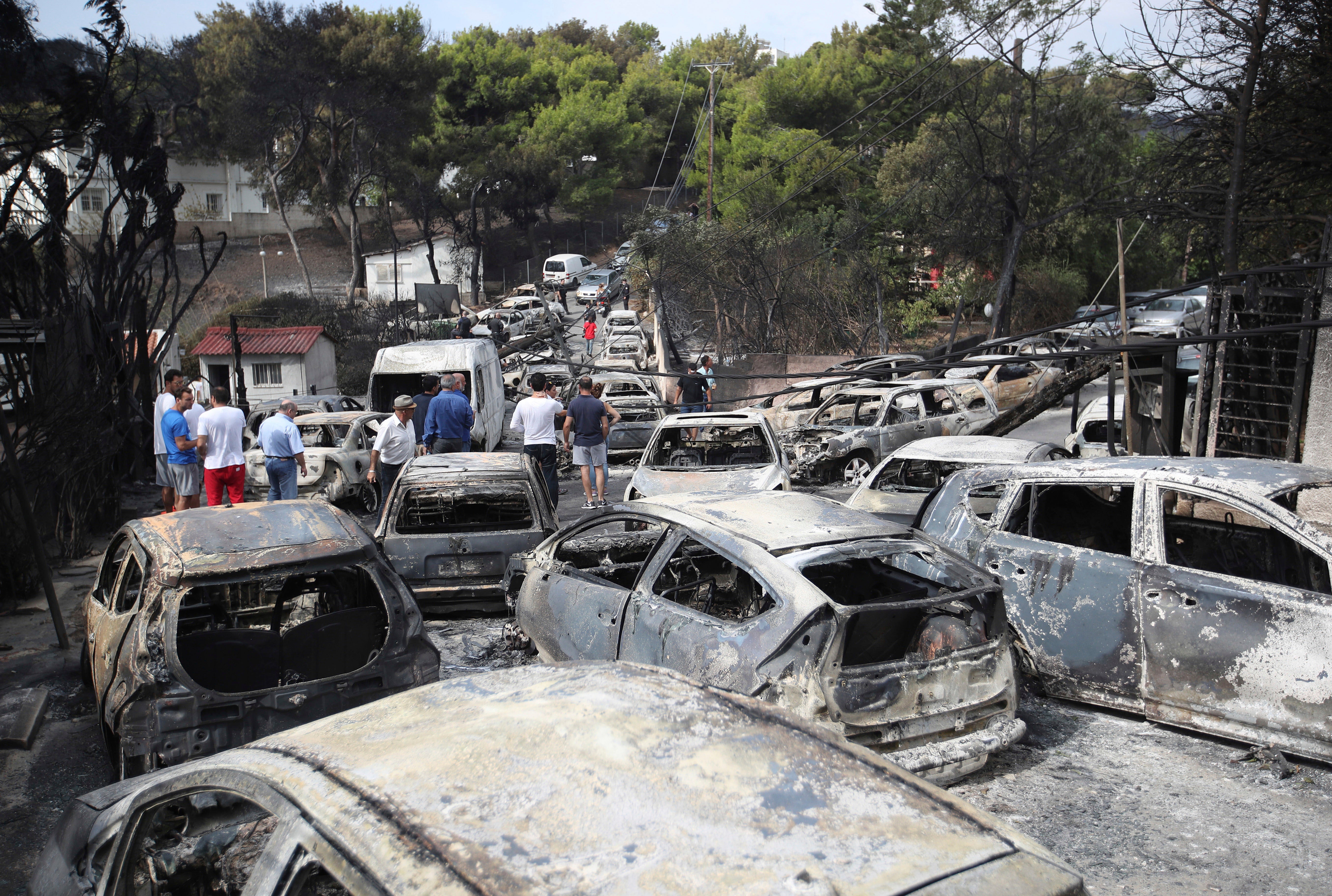 eople stand amid the charred remains of burned-out cars in Mati east of Athens, Greece, Tuesday, July 24, 2018