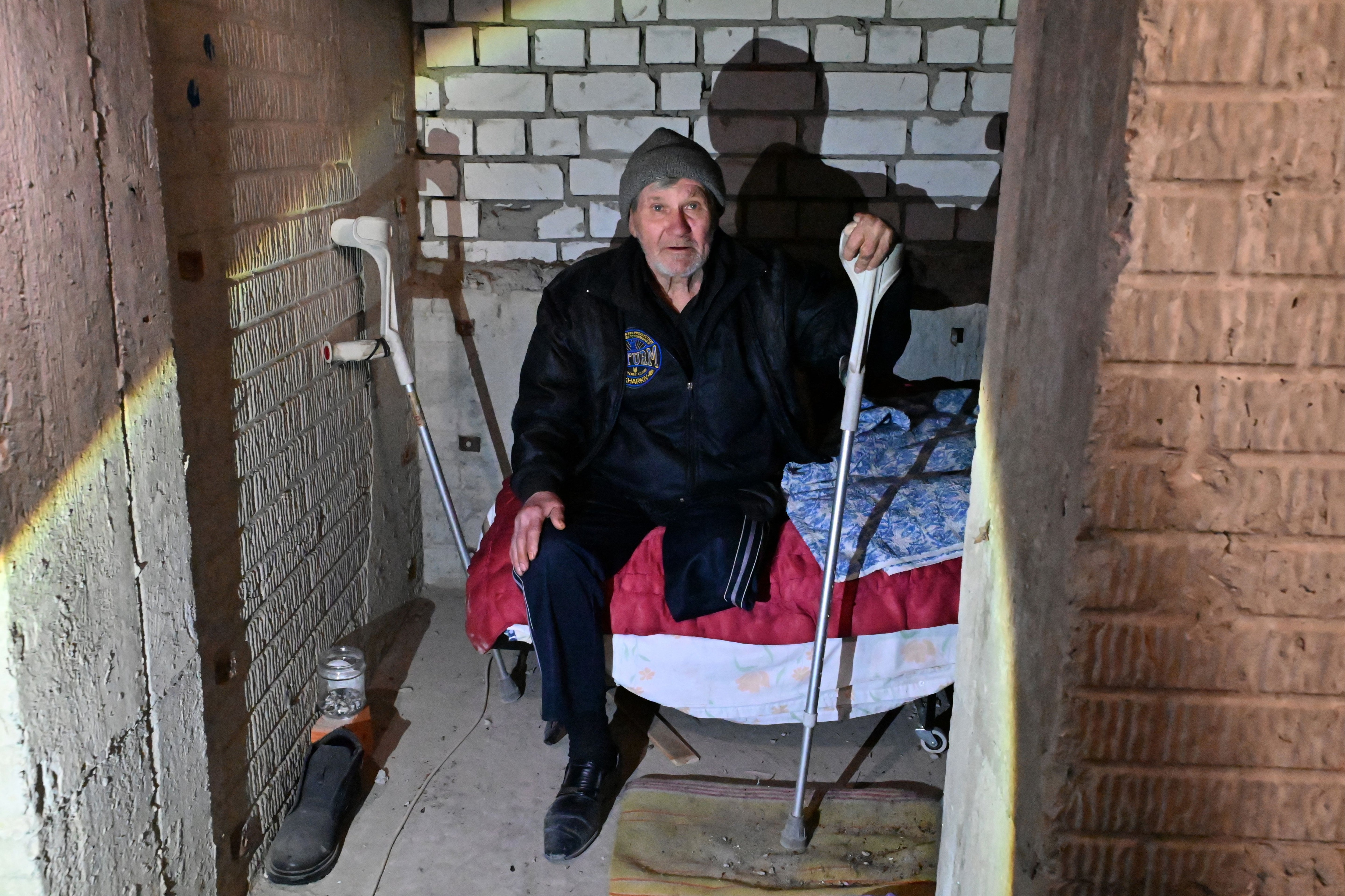 An elderly disabled man sits on a bed as residents of a building, partially destroyed after shelling in Kharkiv
