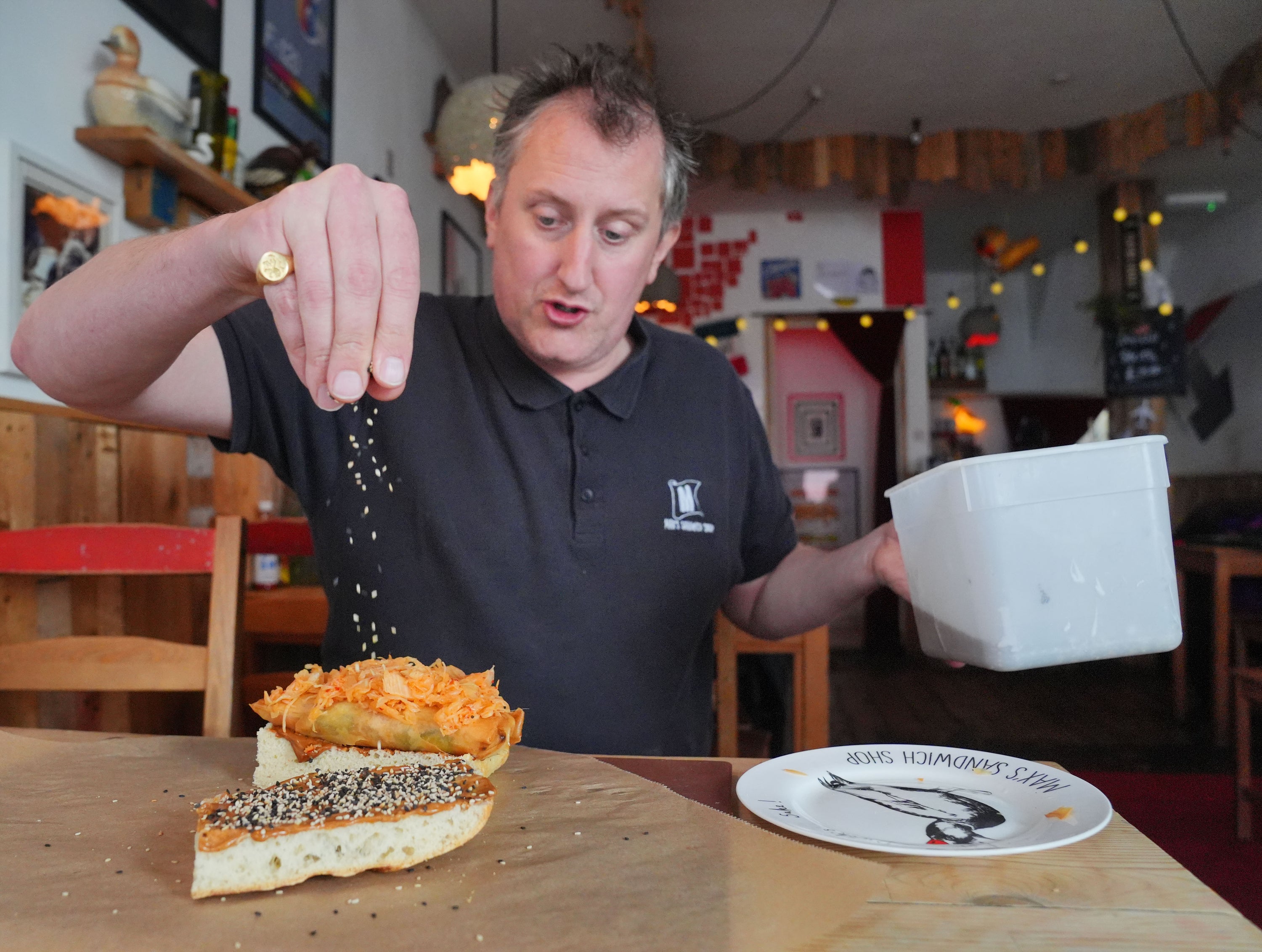 Max Halley sprinkling sesame seeds on the sandwich