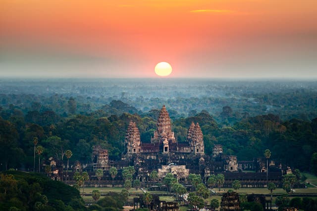 <p>A bird’s eye view of the Angkor Wat temple surrounded by greenery at sunset in Cambodia
</p>