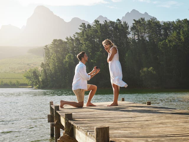 <p>A man proposes to a woman on the dock of a lake. </p>