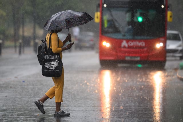 <p>File image: A woman uses an umbrella for shelter as she crosses the road, as torrential rain and thunderstorms </p>