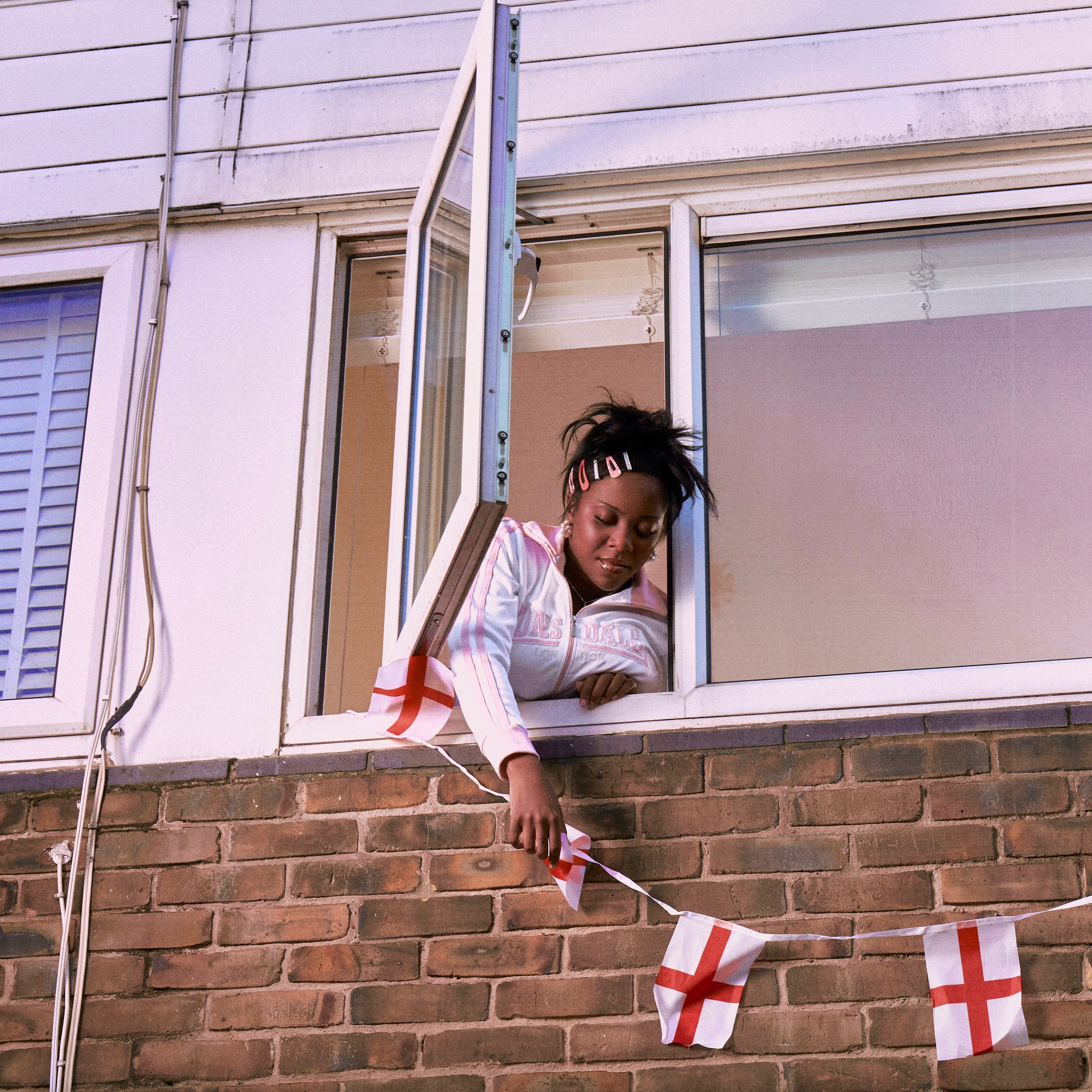 Chinouriri hangs St George’s Cross bunting out the window on her accompanying album artwork