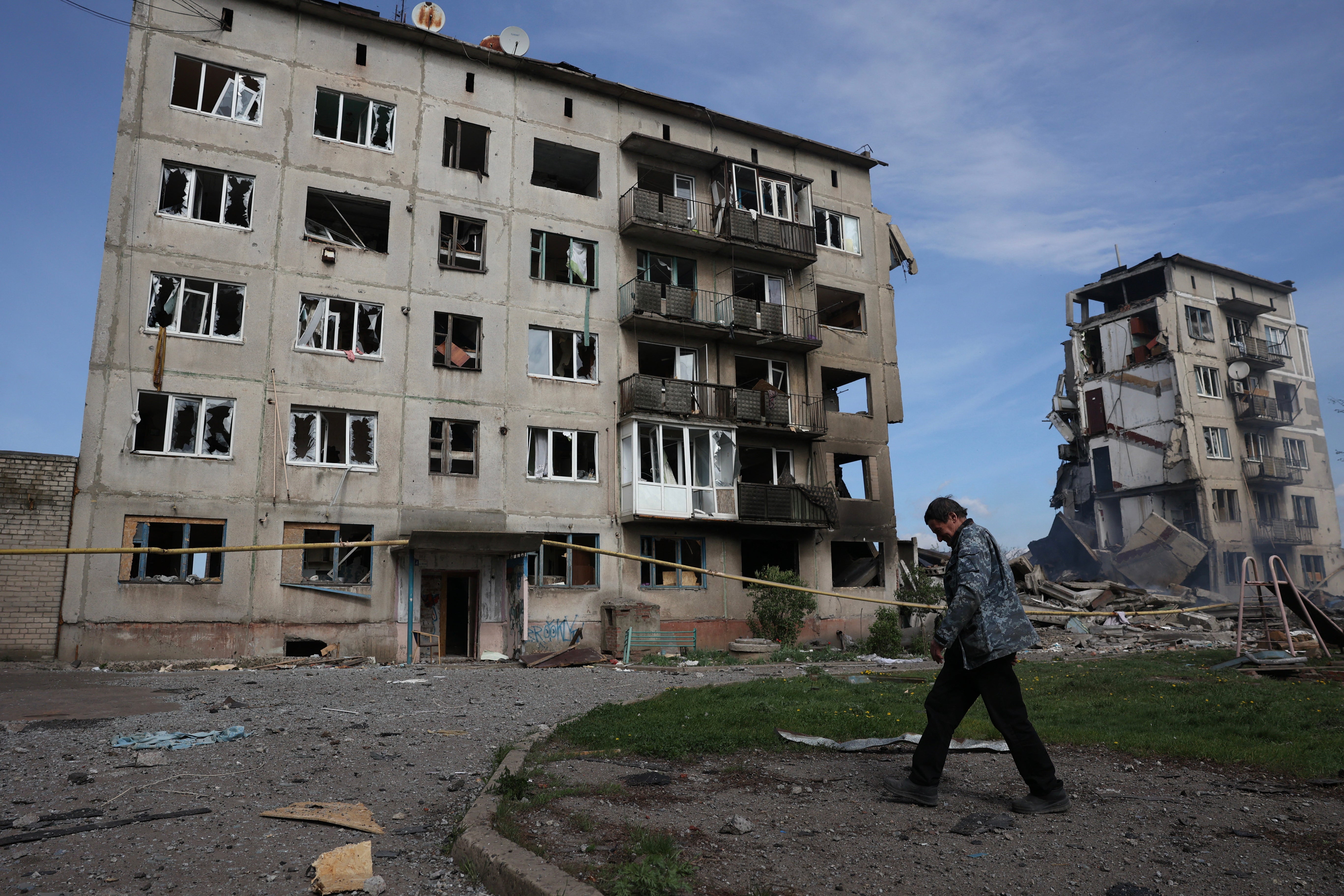 A local resident walks past apartment buildings destroyed by airstrikes in the village of Ocheretyne, days before it was taken by Russian forces
