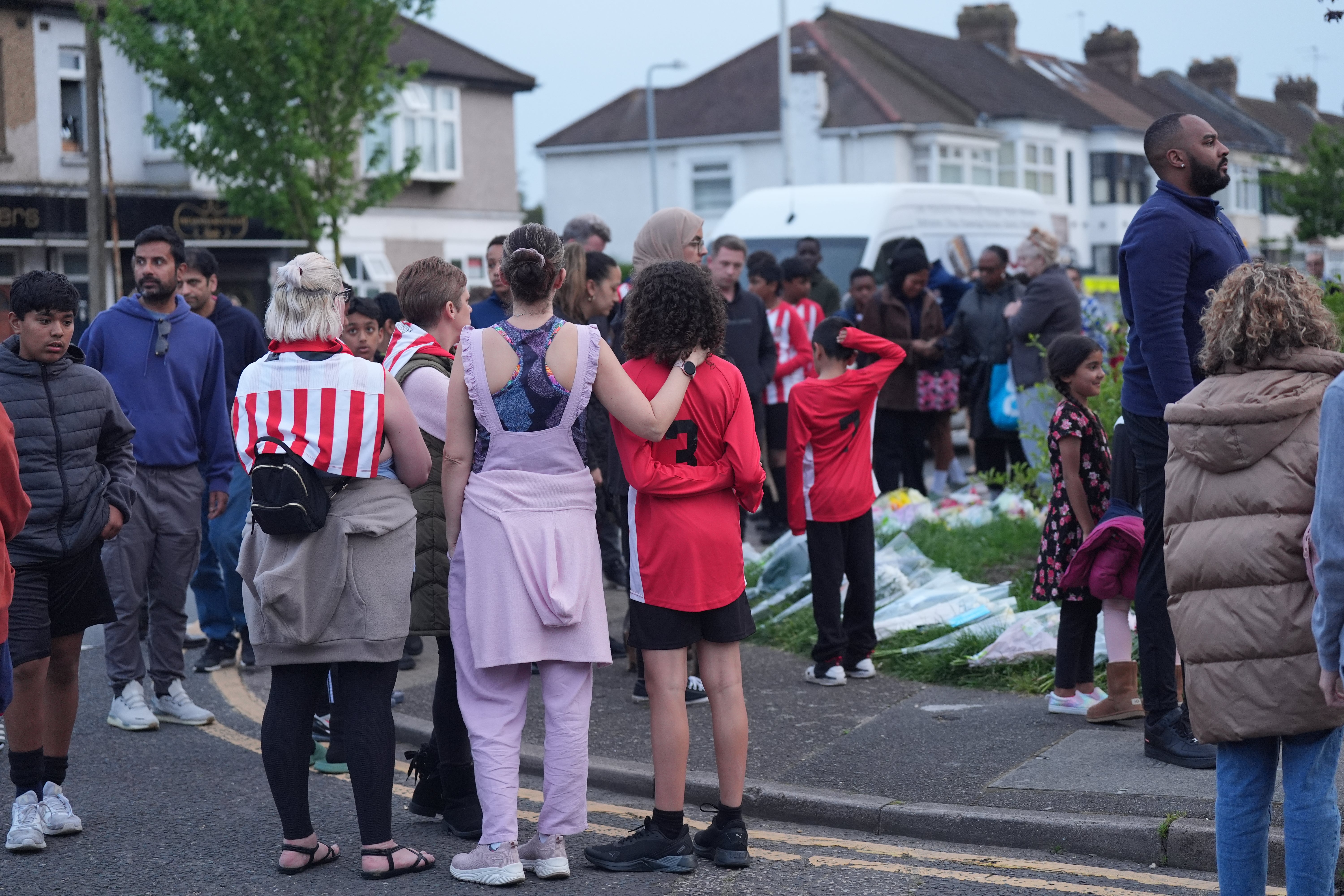 Members of the community, including River Hawks FC, looking at floral tributes in Hainault