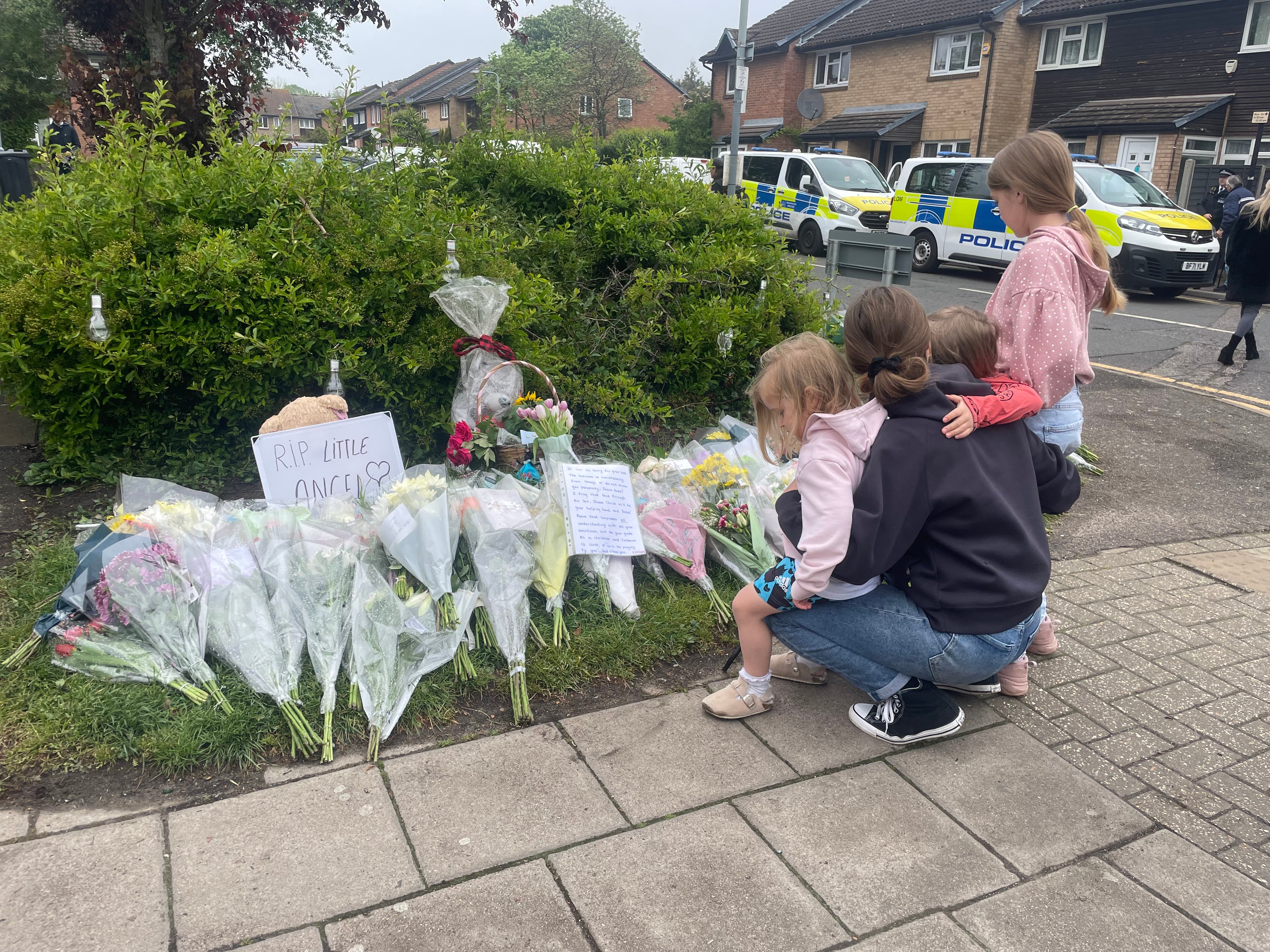 A woman with small children crouches down to read cards left amongst the floral tributes at Laing Close in Hainault for 14-year-old Daniel Anjorin