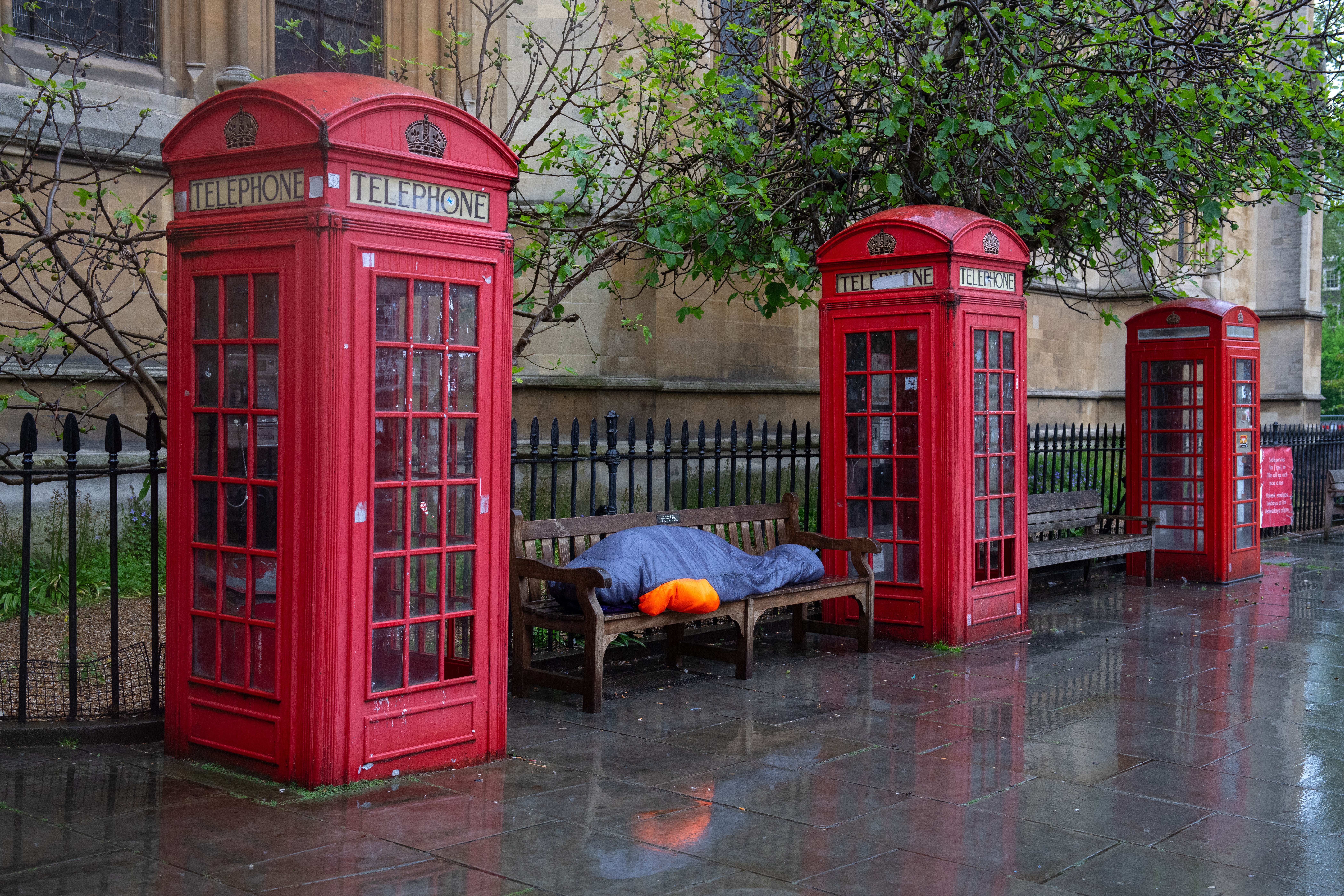 A homeless person sleeps in the rain between phone-boxes in central London