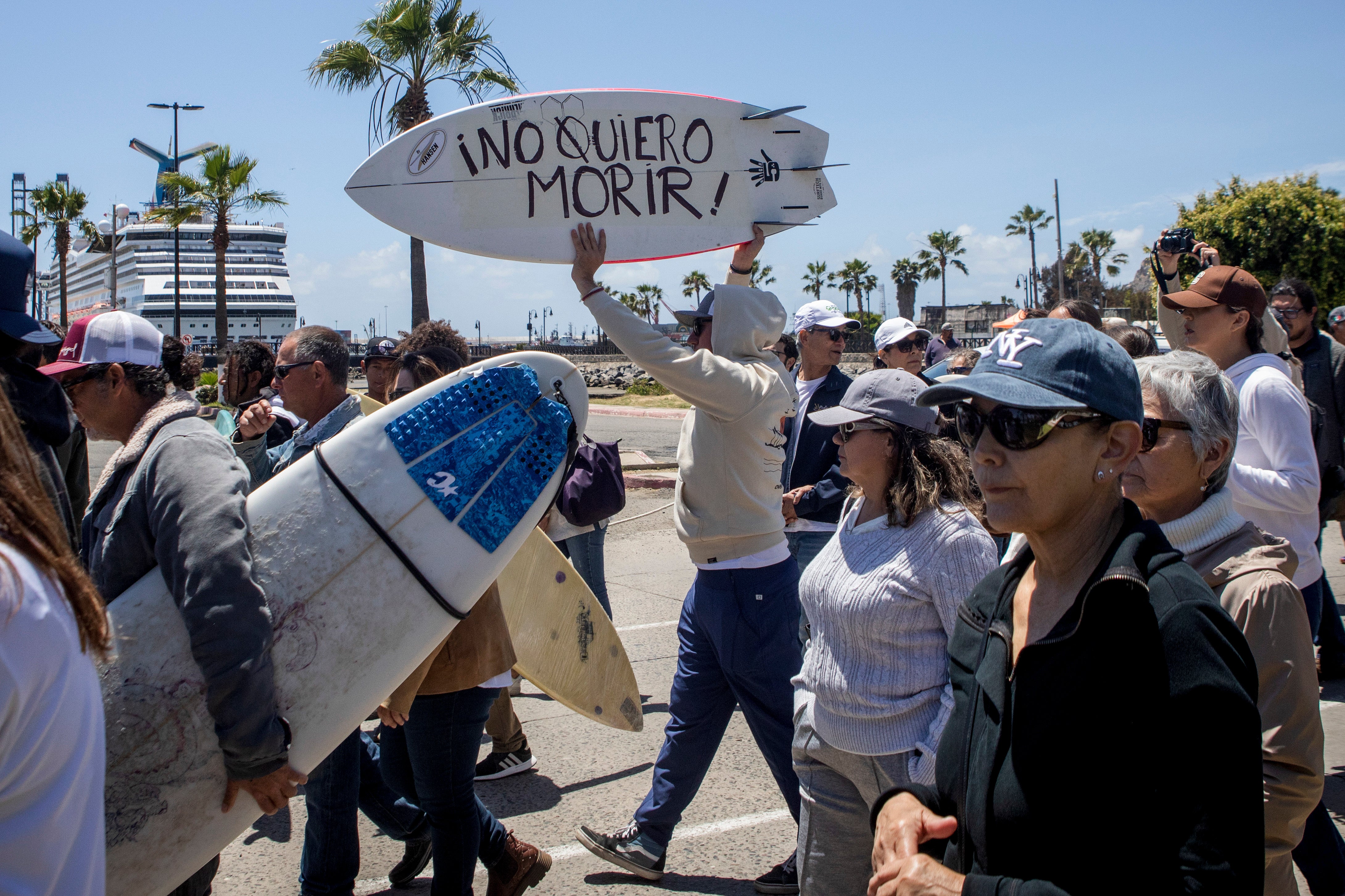 A demonstrator holding a bodyboard with ‘I don't want to die’ written in Spanish as they protest the murders of foreign surfers in Ensenada, Mexico