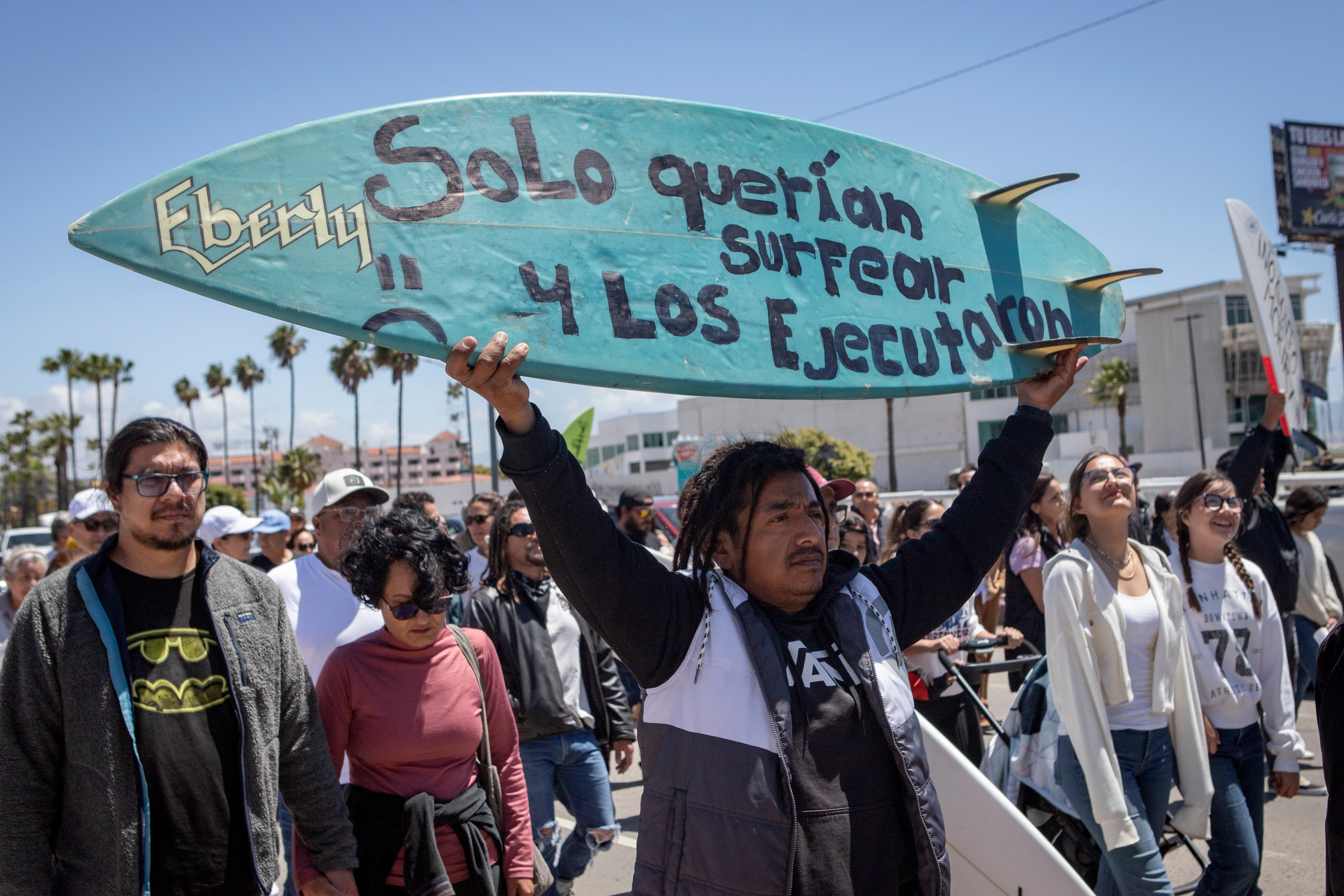 A demonstrator holding a bodyboard written in Spanish ‘They just wanted to surf and they were executed’