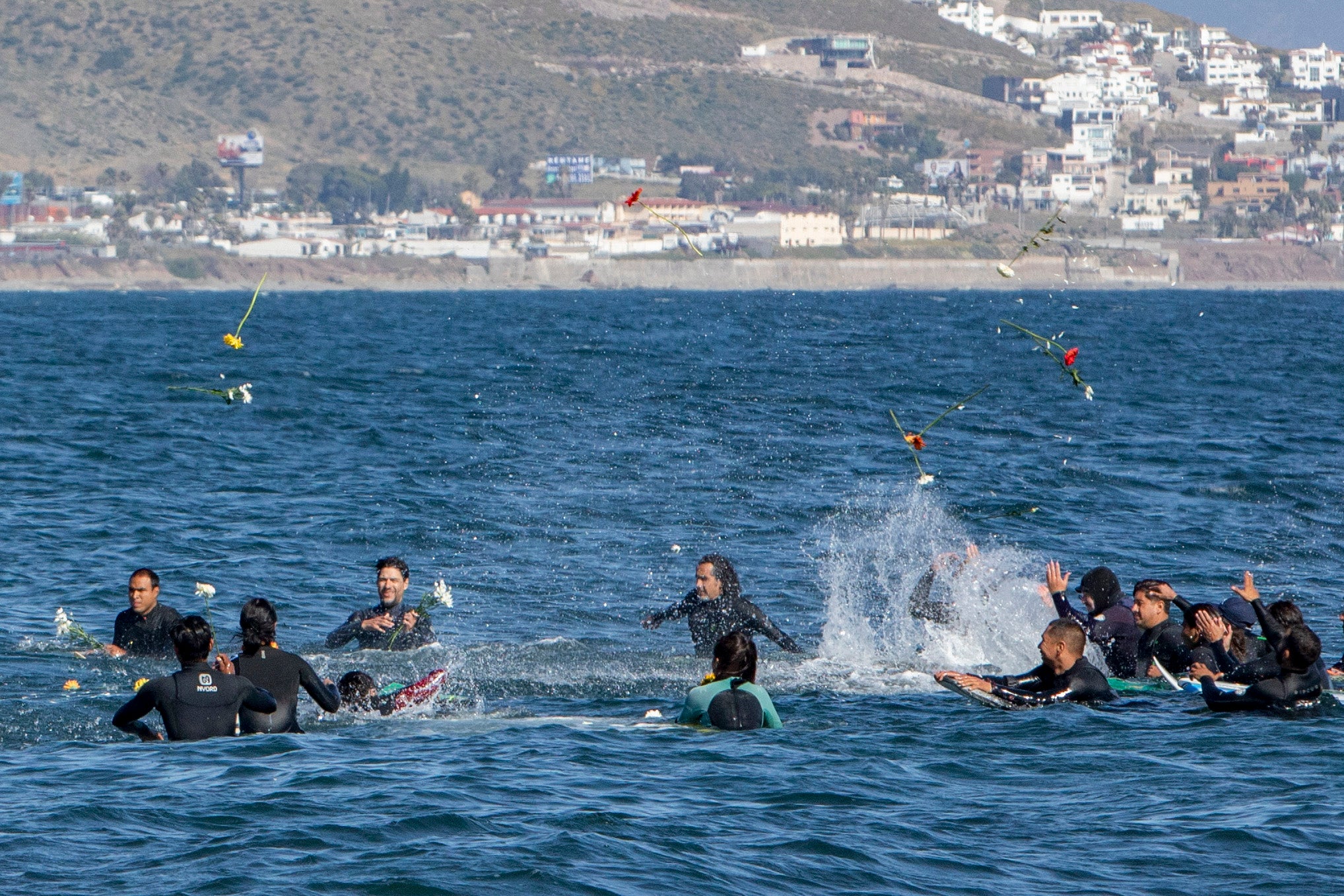 Surfers throw flowers during a paddle-out tribute to the three surfers on Sunday who were killed in Ensenada, Mexico
