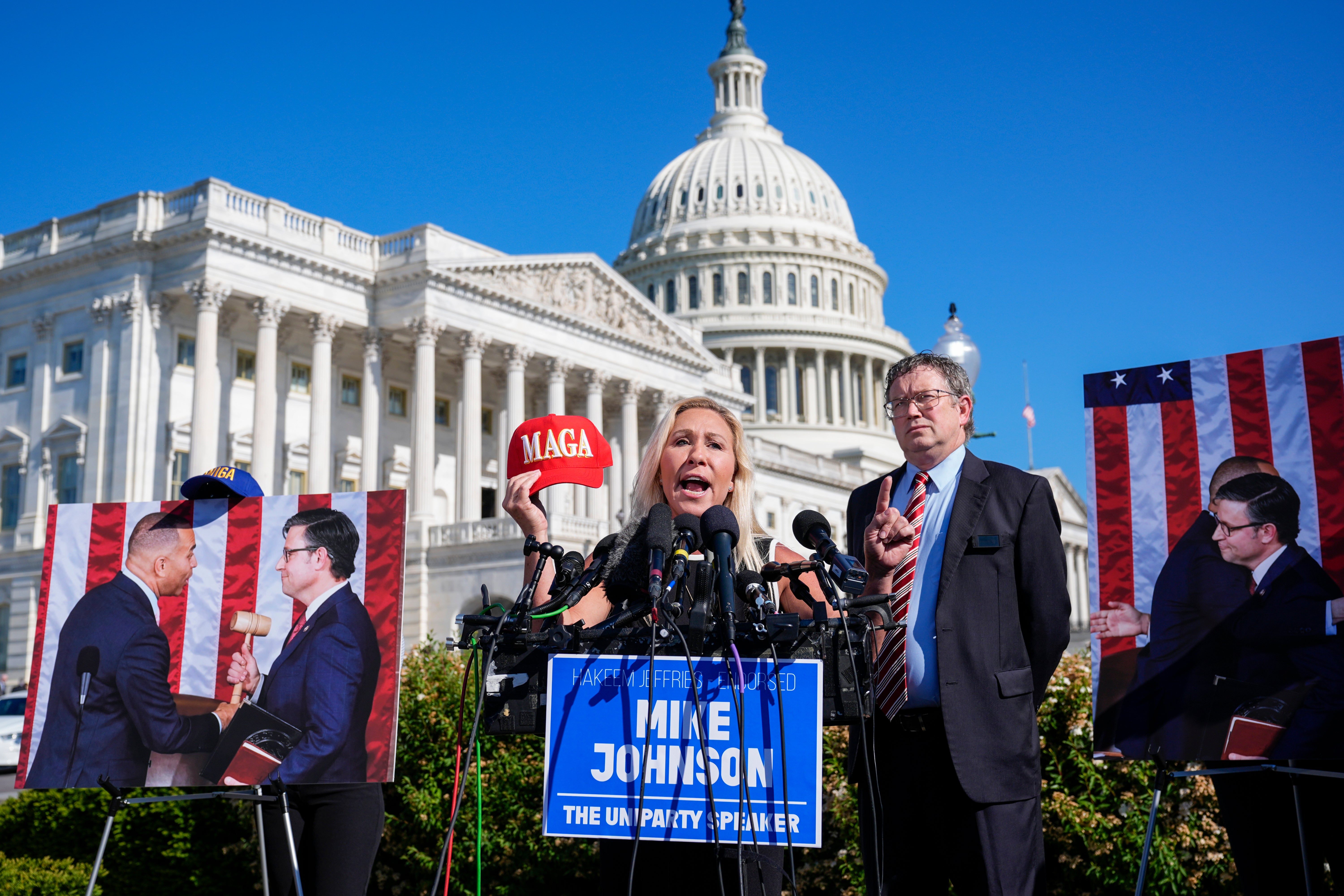 Representatives Marjorie Taylor Greene (centre) and Thomas Massie (right) pictured on 1 May calling for the House to oust Speaker Mike Johnson while standing with pictures of Mr Johnson and Democratic House leader Hakeem Jeffries. The pair has criticised Mr Johnson for working with Democrats