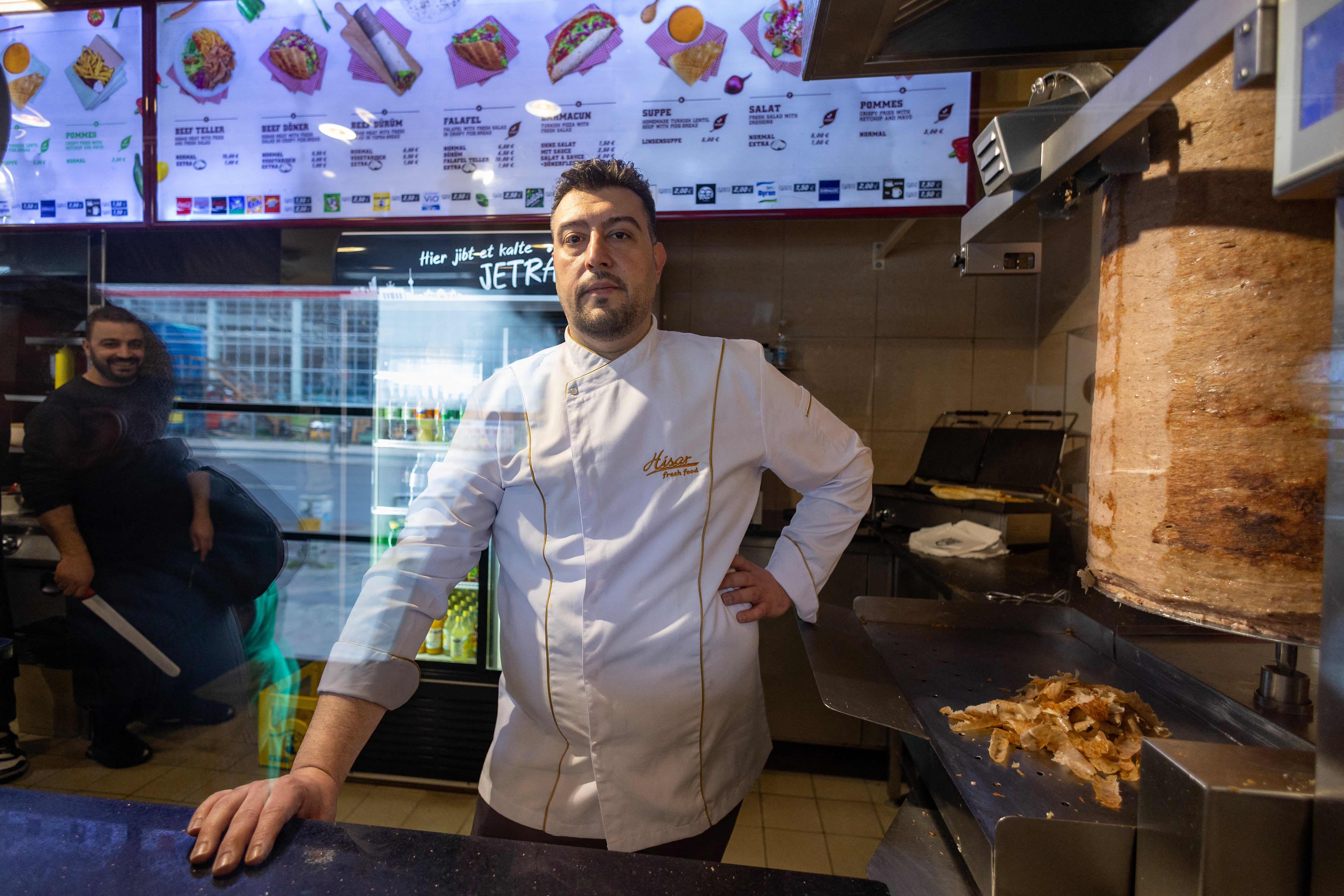Arif Keles, a third-generation barbecue snack bar owner poses next to the doner kebab meat skewer in Berlin