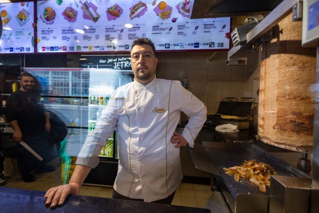 <p>Arif Keles, a third-generation barbecue snack bar owner poses next to the doner kebab meat skewer in Berlin </p>