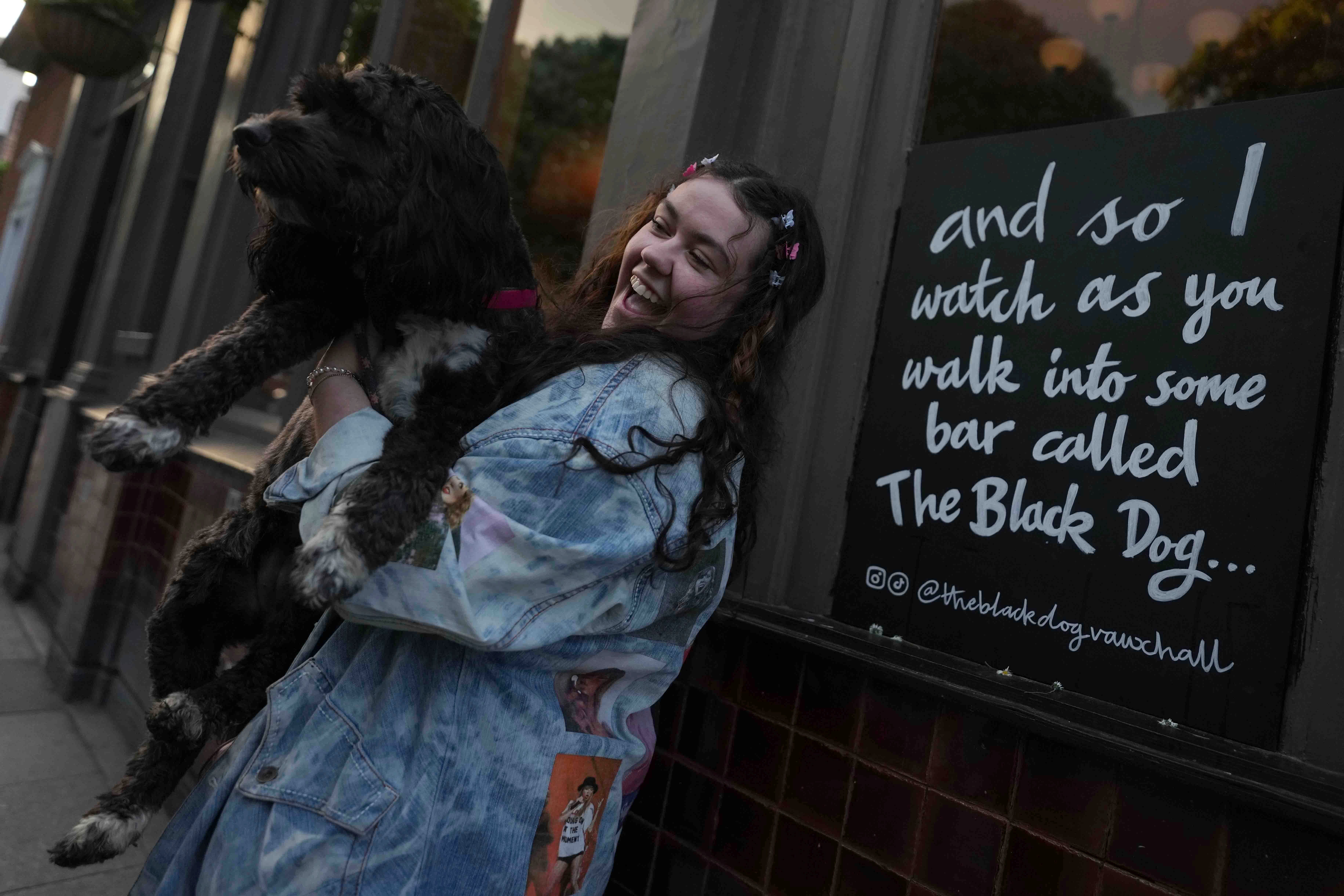 Taylor Swift fan Brodie MacArthur from east London poses with a friend's dog next to a sign featuring Taylor Swift lyrics outside The Black Dog pub in Vauxhall, London
