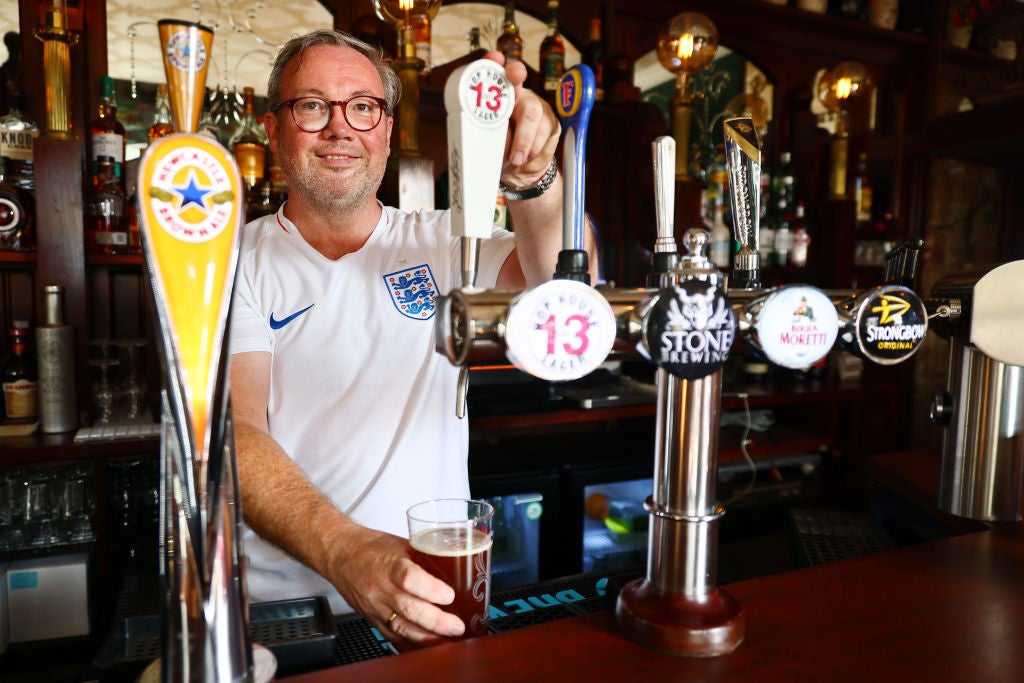 A bartender wearing an England football shirt pours a pint at a pub