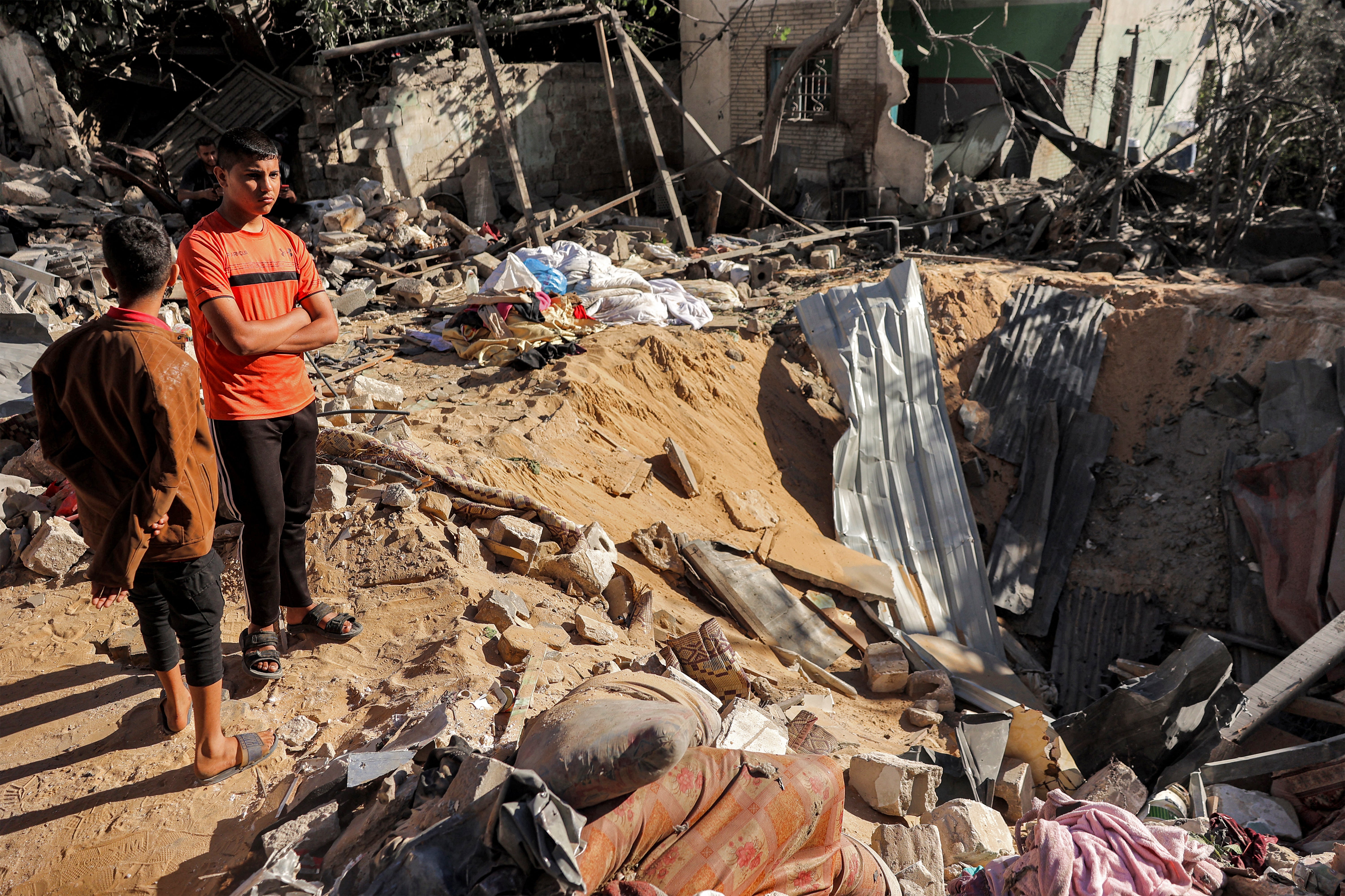 Children stand by an impact crater left by Israeli bombardment in Rafah in the southern Gaza Strip