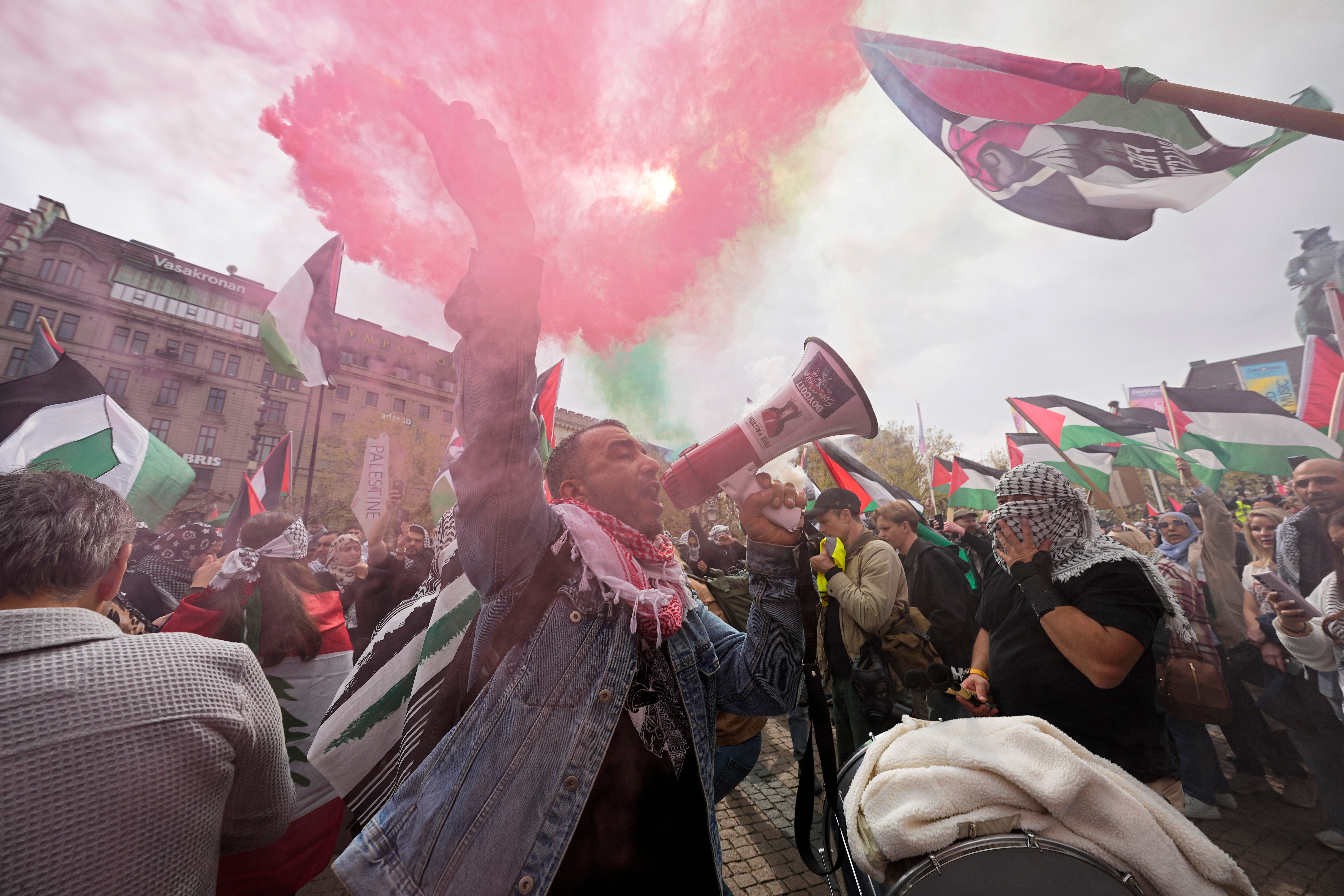 A protestor shouts through a megaphone as smoke canisters in the colours of the Palestinian flag are set off during pro-Palestine protests in Malmo, Sweden