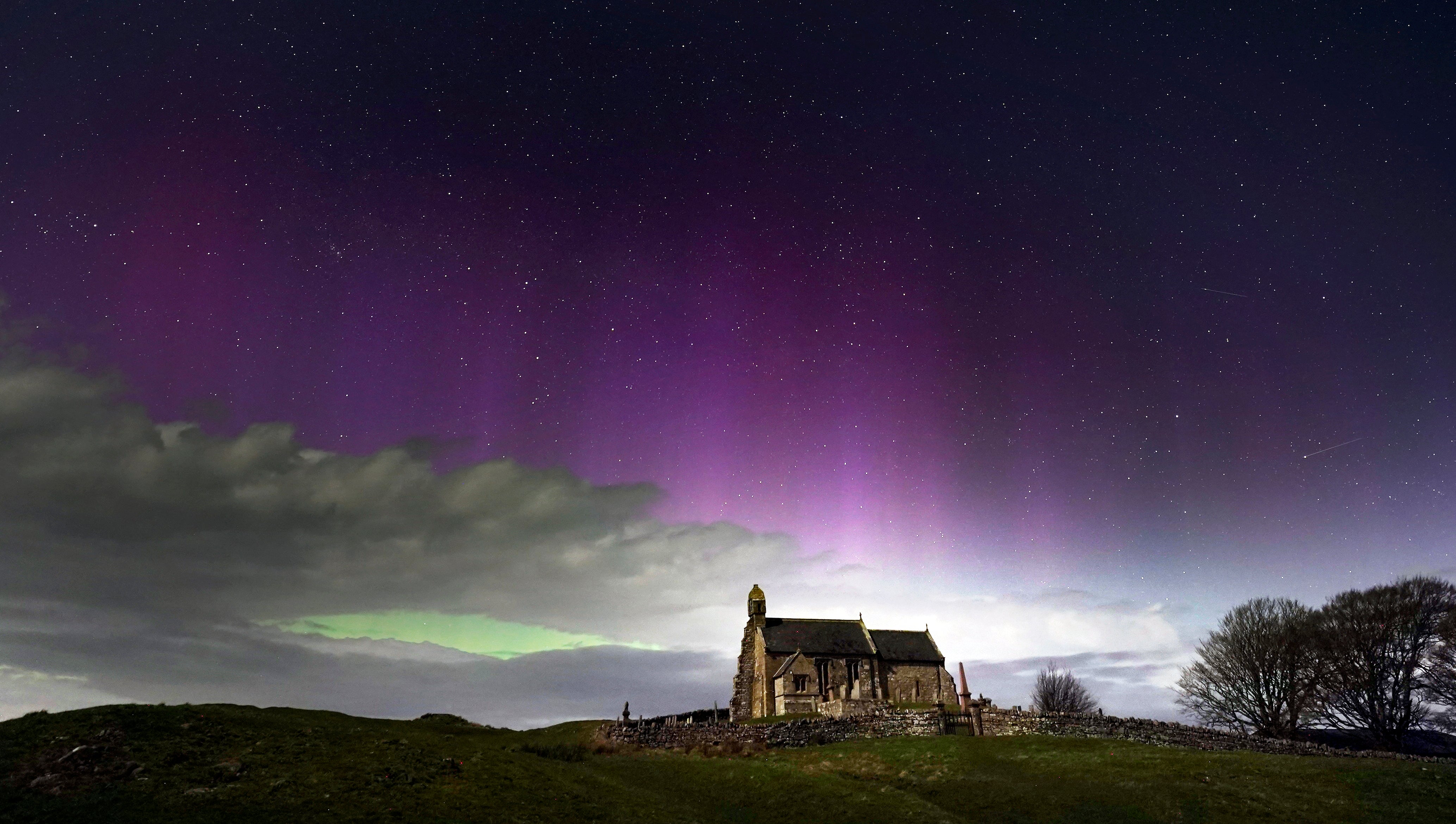 The aurora borealis, also known as the Northern Lights, illuminate the sky just before midnight over St Aidan's church in Thockrington, Northumberland