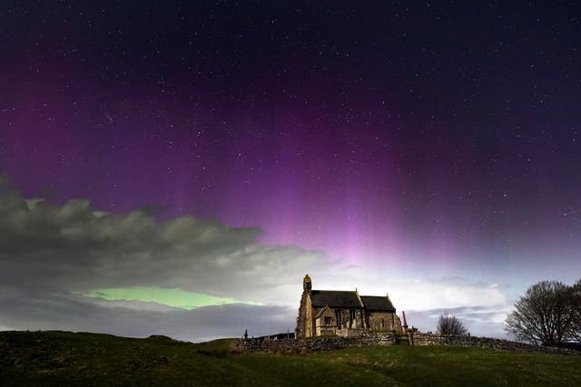 <p>The aurora borealis, also known as the Northern Lights, illuminate the sky just before midnight over St Aidan's church in Thockrington, Northumberland</p>