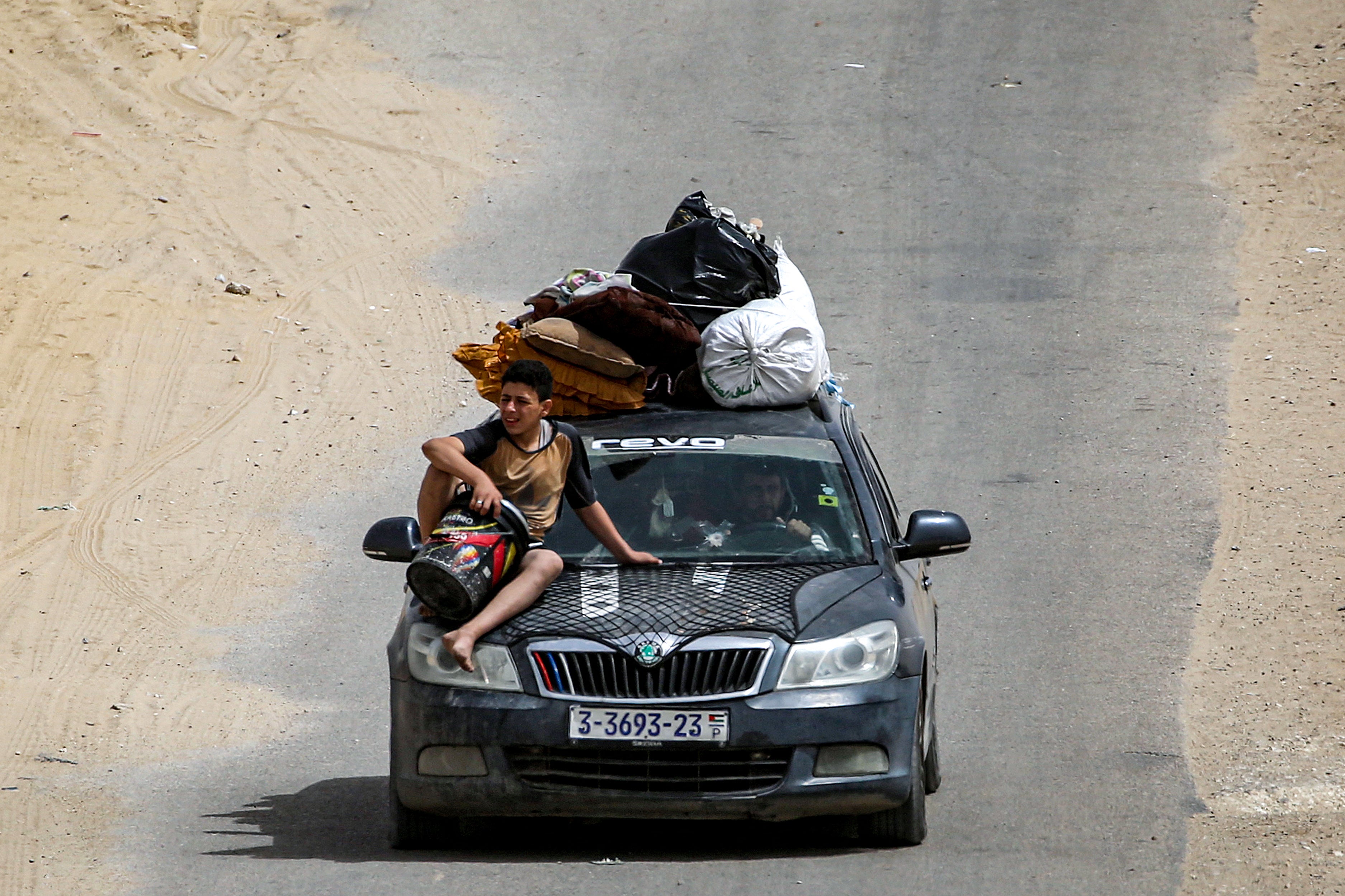 A boy sits on the hood of a vehicle loaded with belongings as members of a Palestinian family flee bound for Khan Yunis
