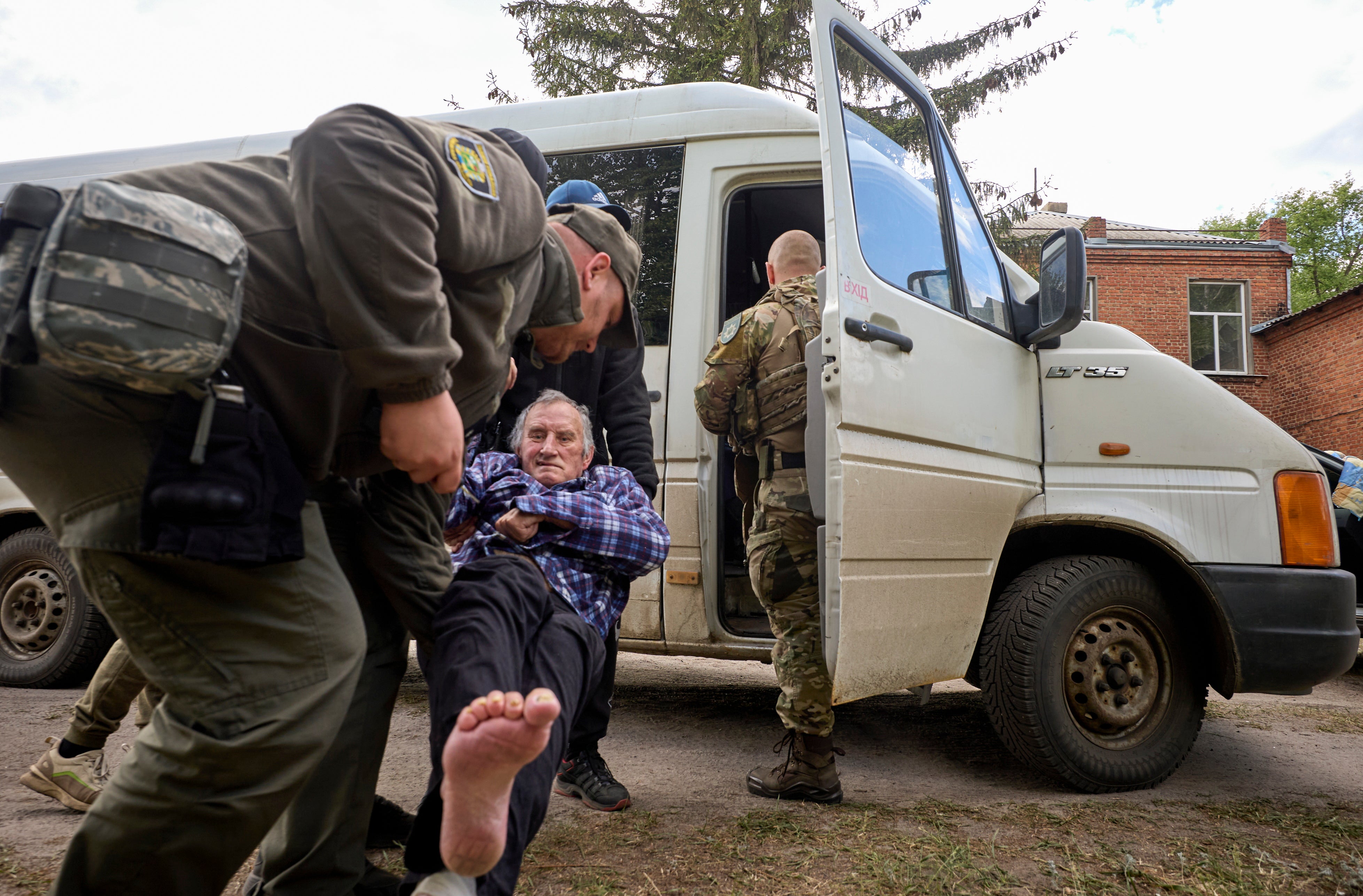 Policemen and volunteers load an elderly man onto a van as they evacuate locals from the Buhaivka village near Volchansk, Kharkiv area