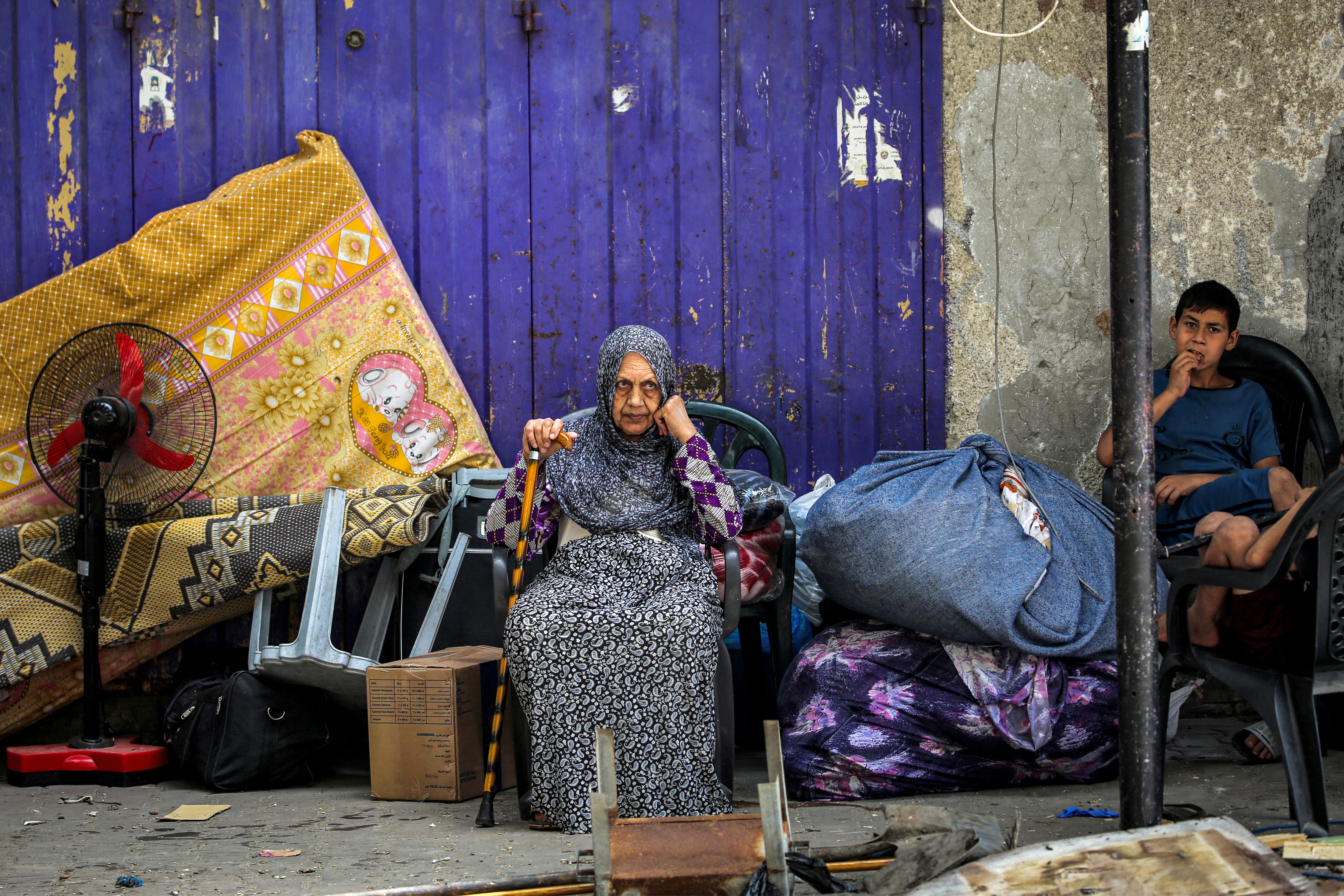 An elderly woman and child wait with belongings before evacuating from Rafah
