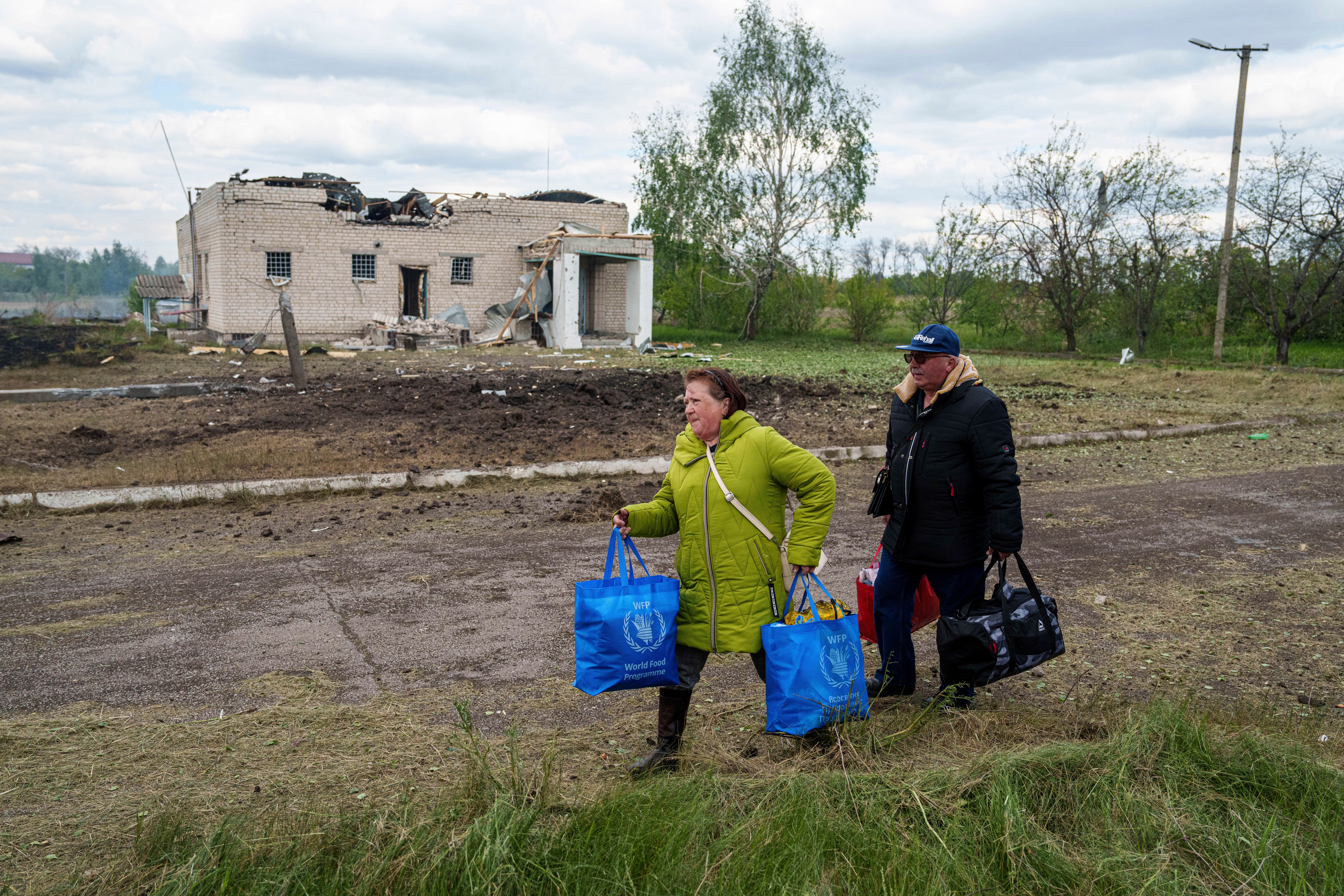 People walk with their belongings to the evacuation point in front of a building that was damaged by a Russian airstrike in Vilcha, near Vovchansk