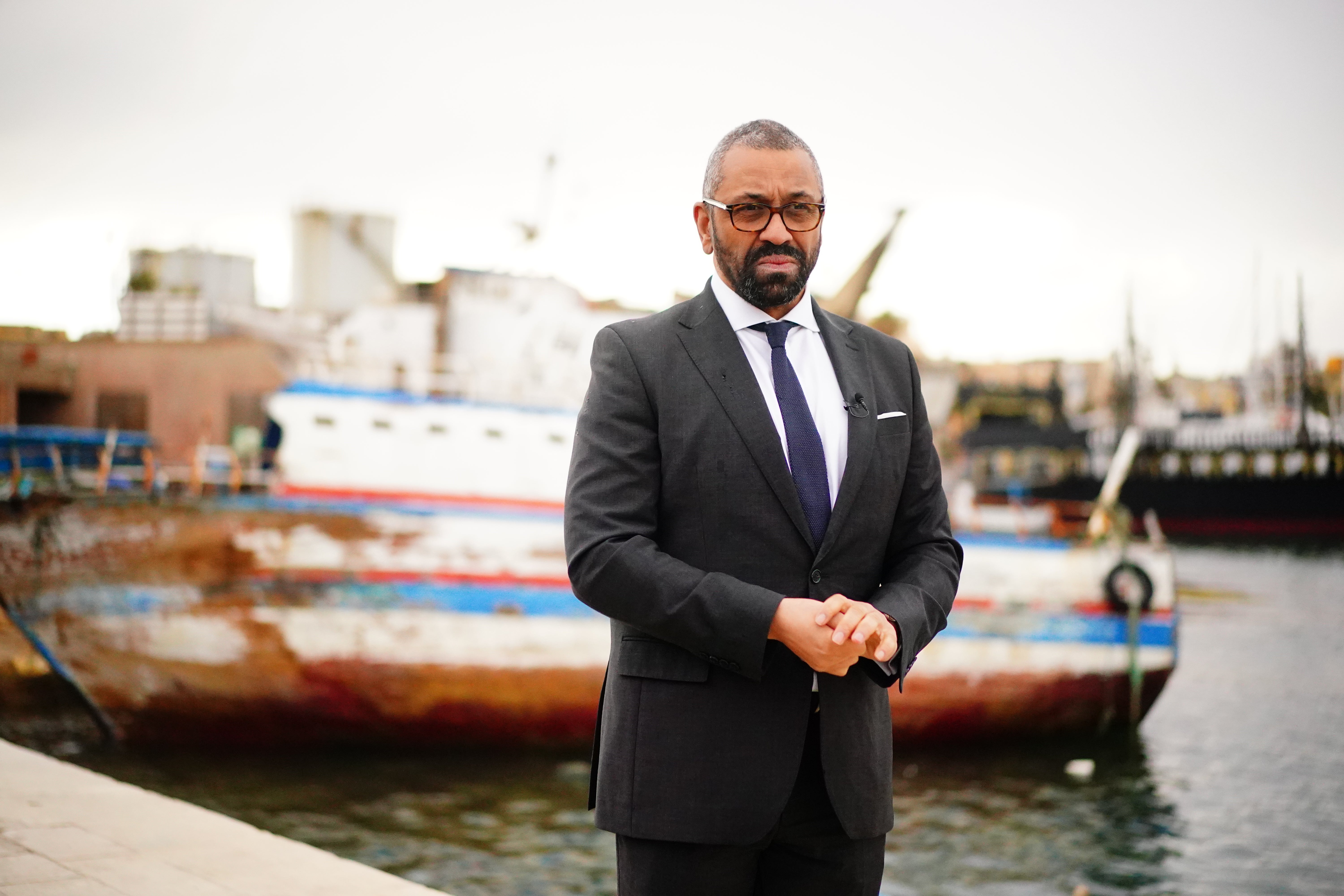 Home Secretary James Cleverly standing in front of a discarded migrant boat in Lampedusa Port, April 2024