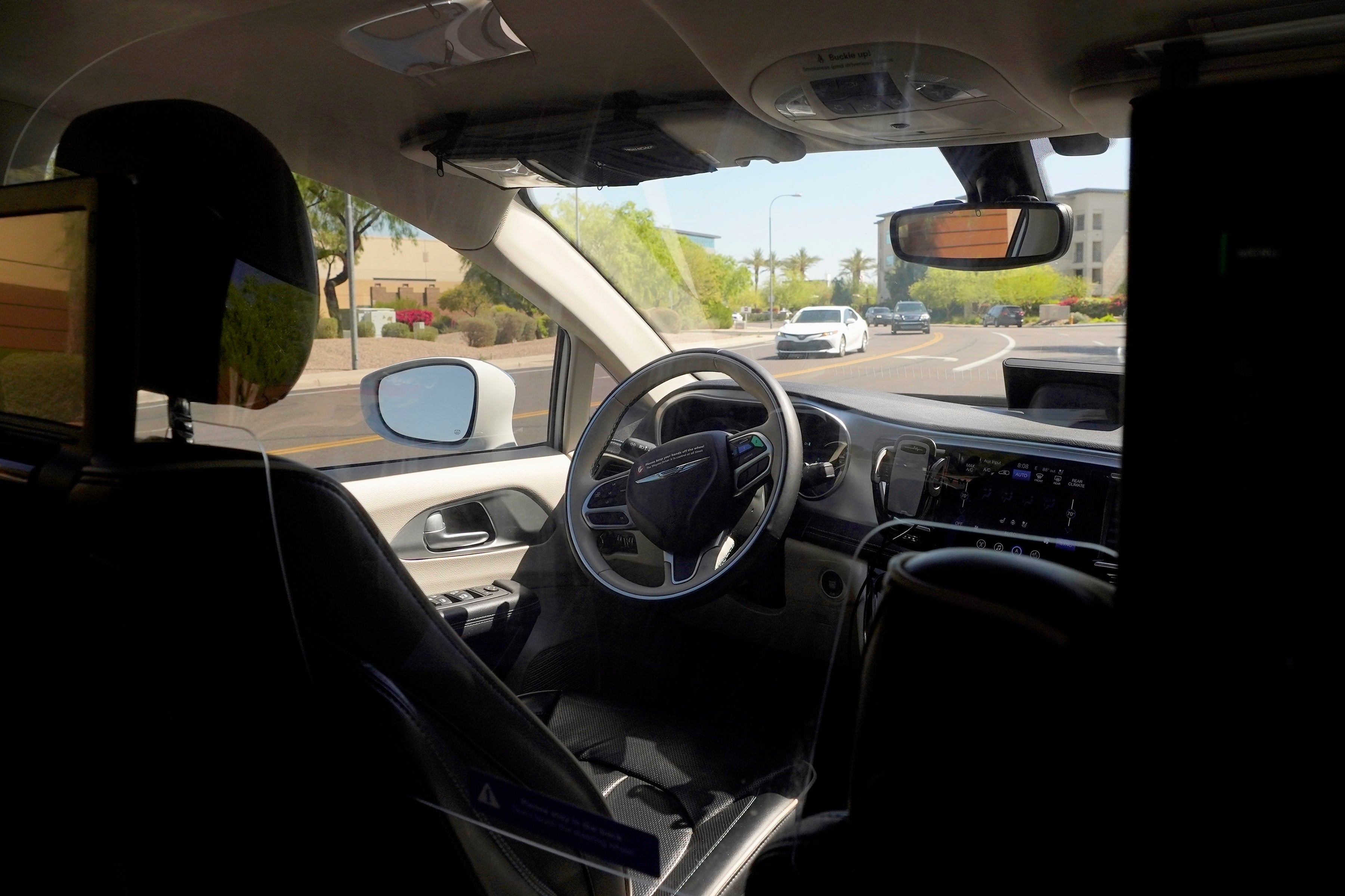 A Waymo minivan moves along a city street as an empty driver's seat and a moving steering wheel drive passengers during an autonomous vehicle ride, on April 7, 2021, in Chandler, Arizona