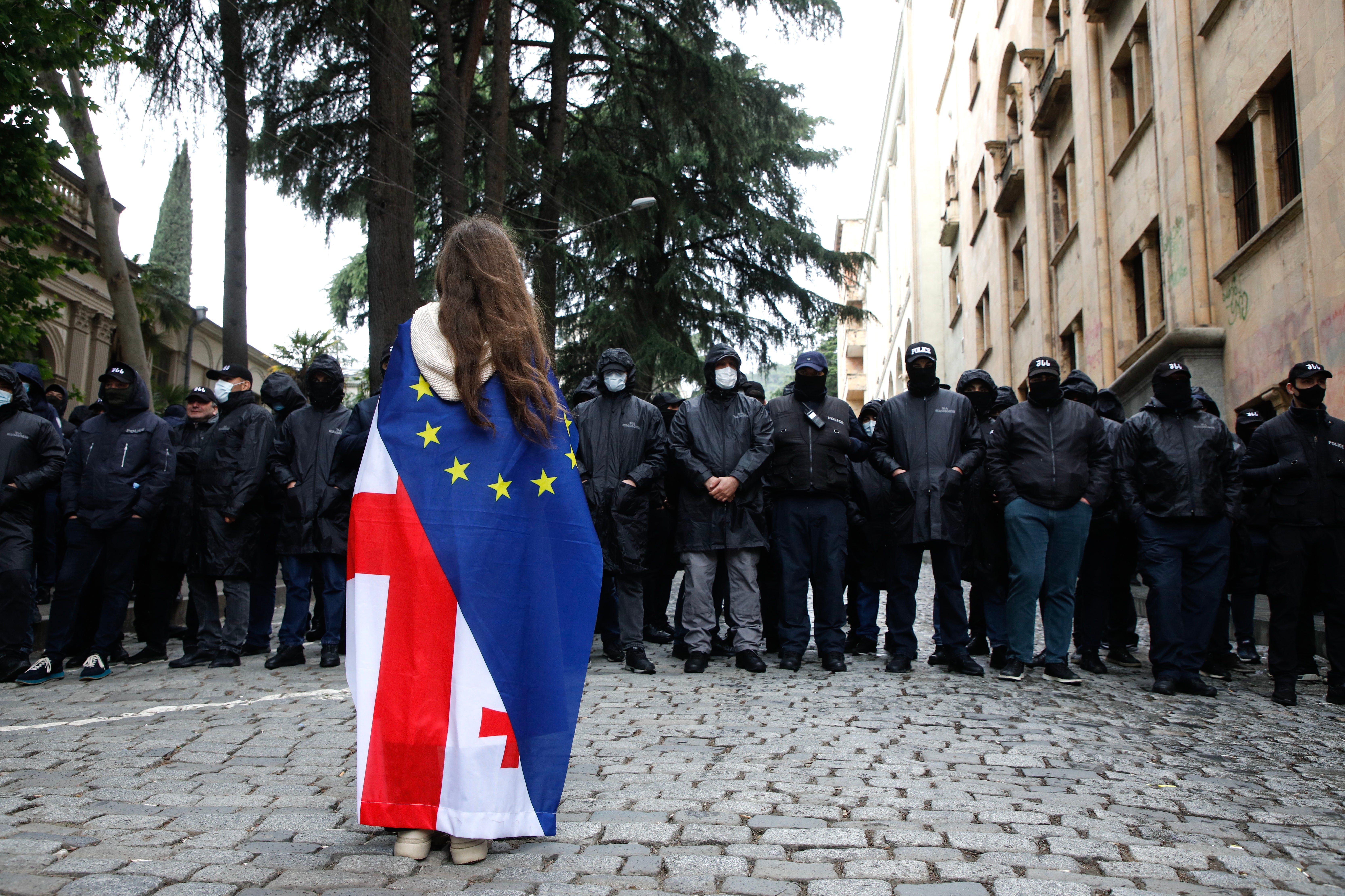 A protester wearing a Georgian and European flag faces off policemen blocking a street during a rally against a draft bill on 'foreign agents' near the Parliament building in Tbilisi, Georgia, 14 May 2024